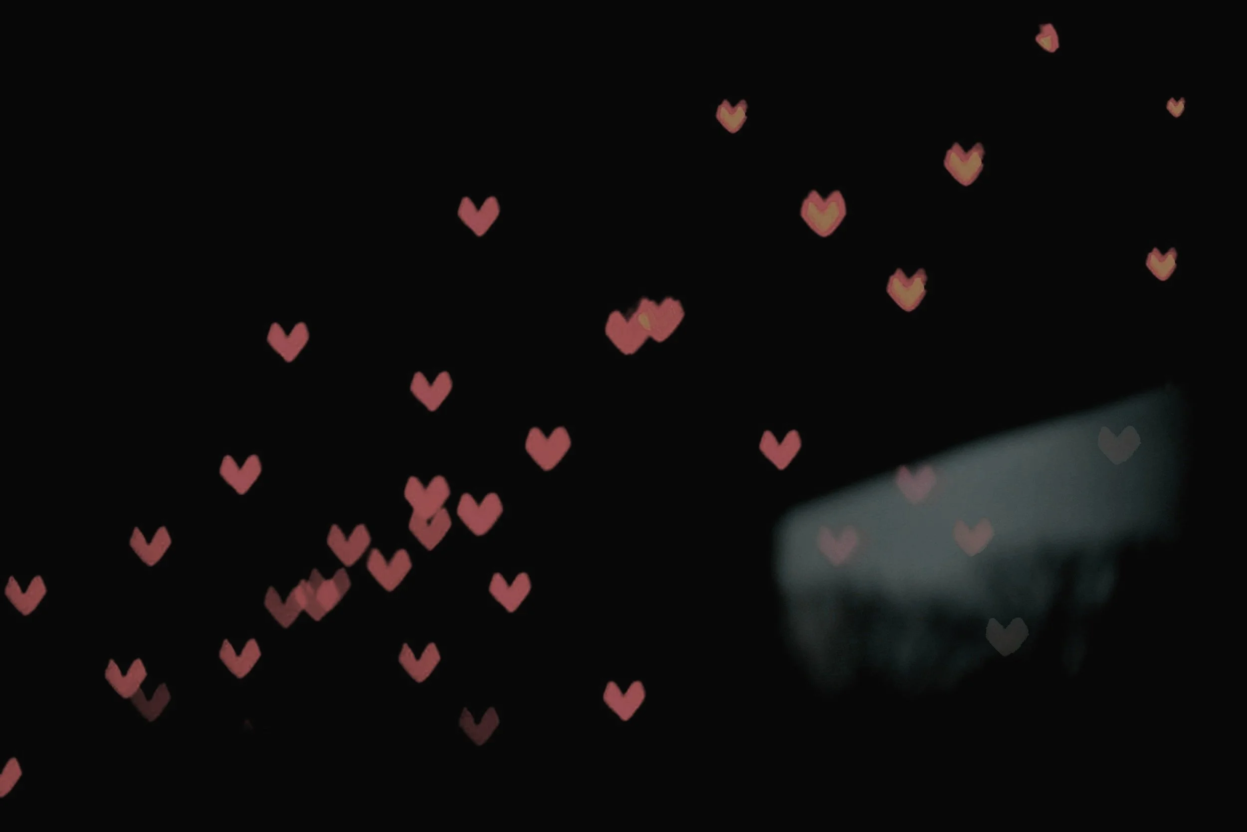 Pink heart-shaped lights on a dark background creating a bokeh effect.