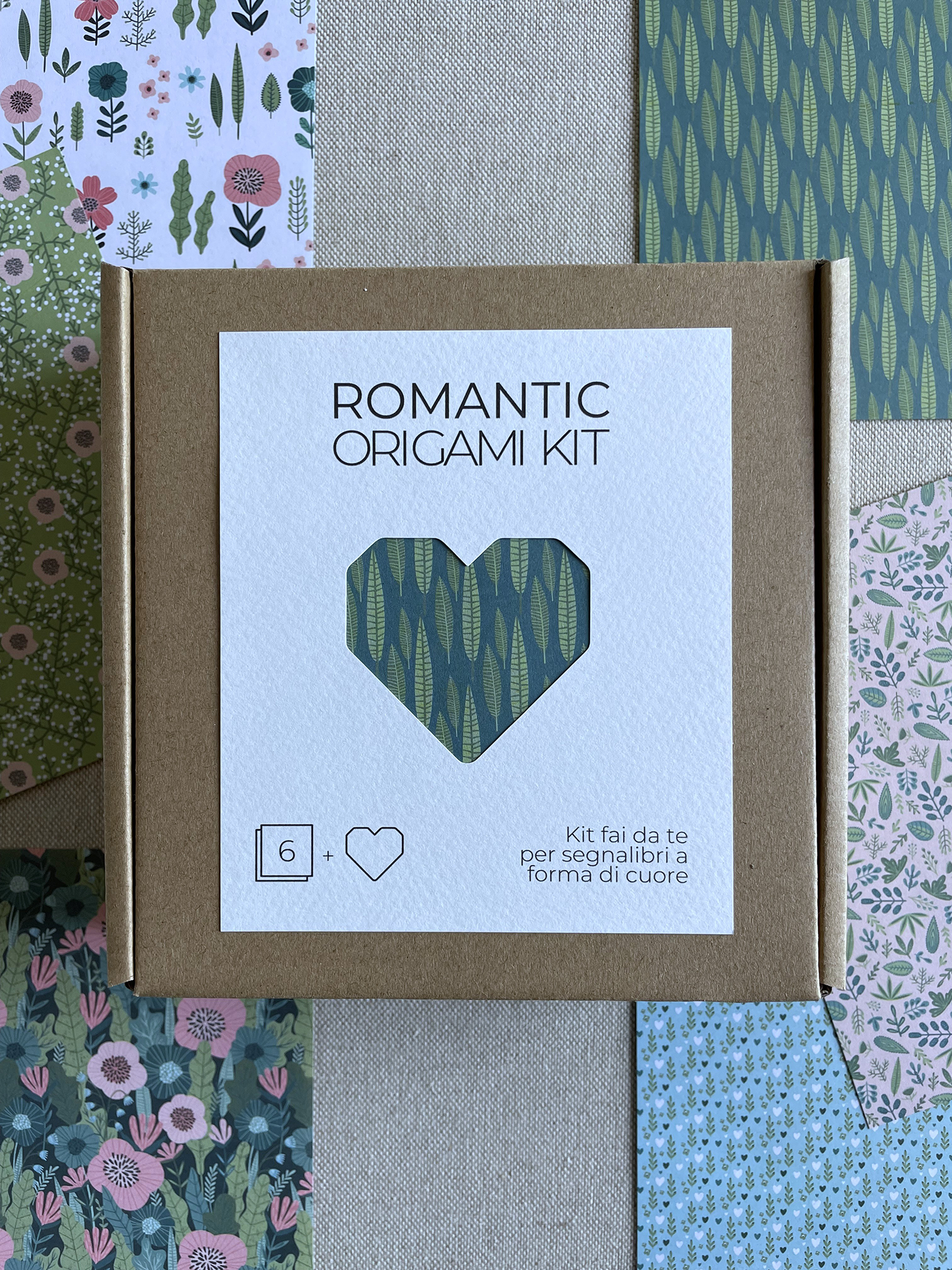 Confezione di kit origami romantici con cuore, su sfondo di vari fogli decorativi con motivi floreali e vegetali.