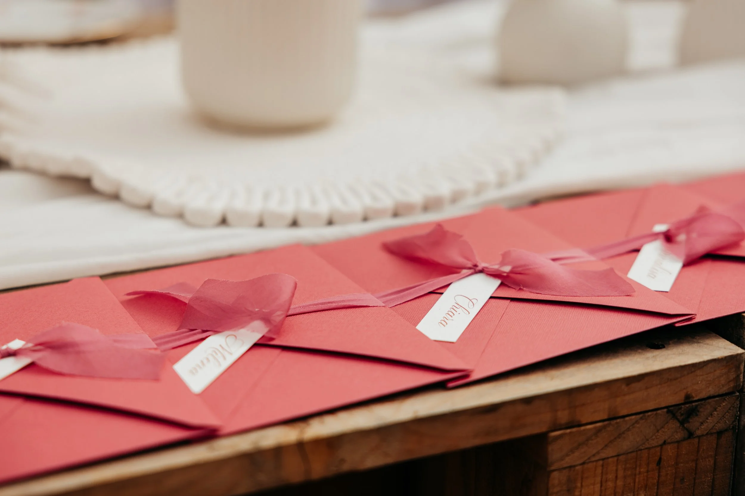 Centinaia di partecipazioni di matrimonio di colore rosa, decorati con fiocchi di seta, traghetta con nome degli invitati, disposti su un tavolo di legno.