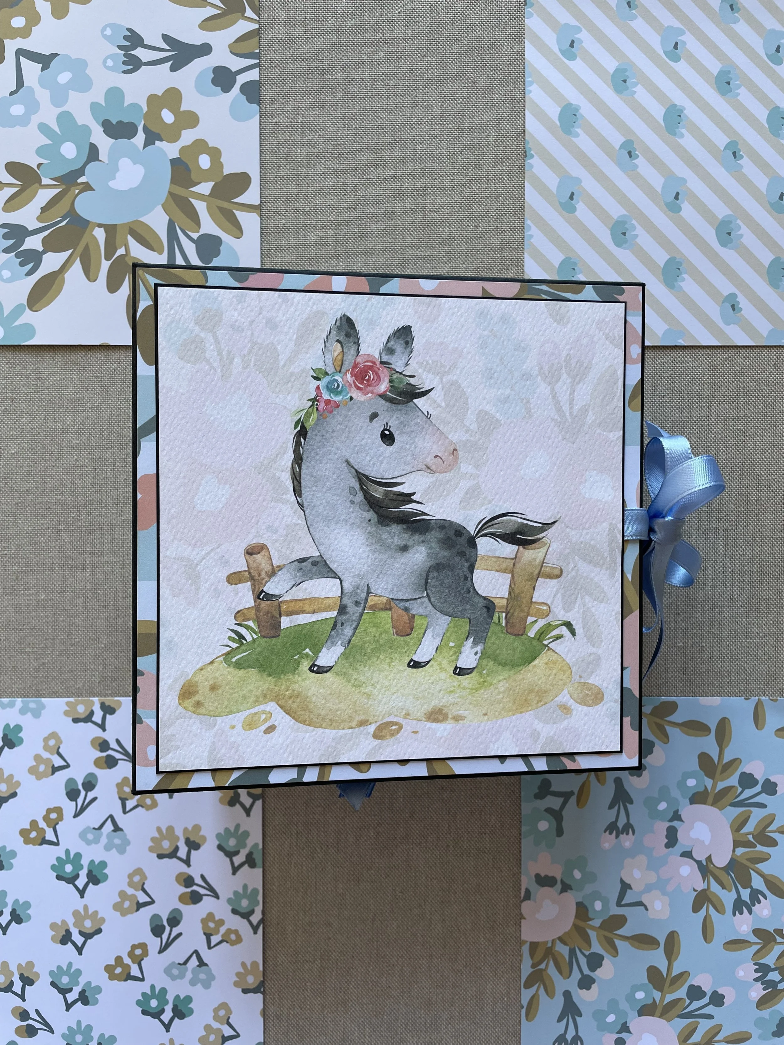 Album per foto, modello Curvy, di forma quadrata, a tema cavalli e motivi floreali. Realizzato completamente a mano. si chiude con un fiocco il raso azzurro. regalo nascita, battesimo bambini.