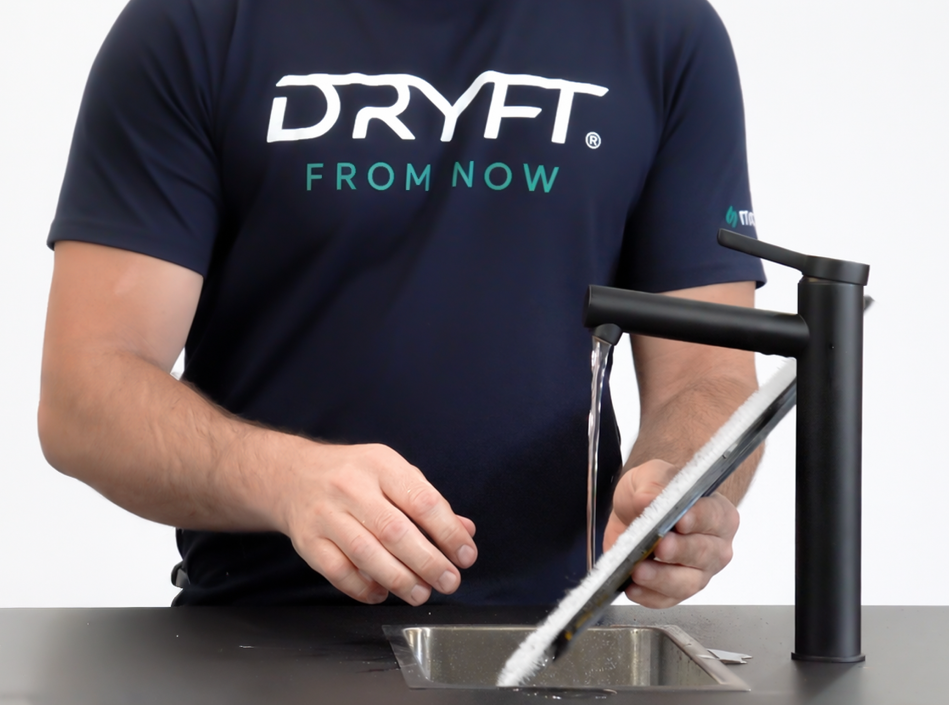 DRYFT team member rinsing the white Melamine Cleaning Pad under running water while it remains attached to the pad holder, removing dirt residue after use.