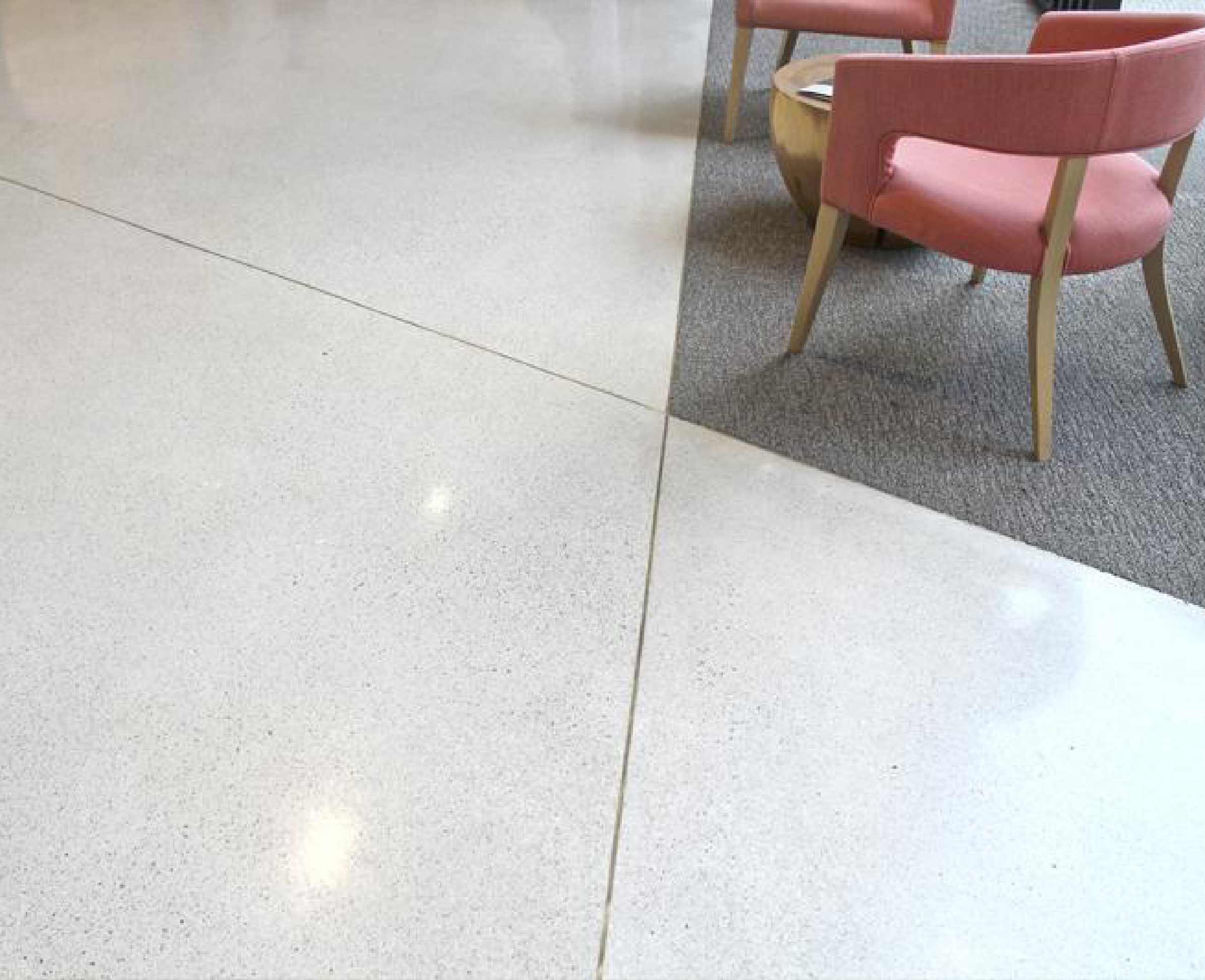 Smooth, light grey sealed concrete flooring in a modern interior, featuring a polished finish and pink upholstered chairs.