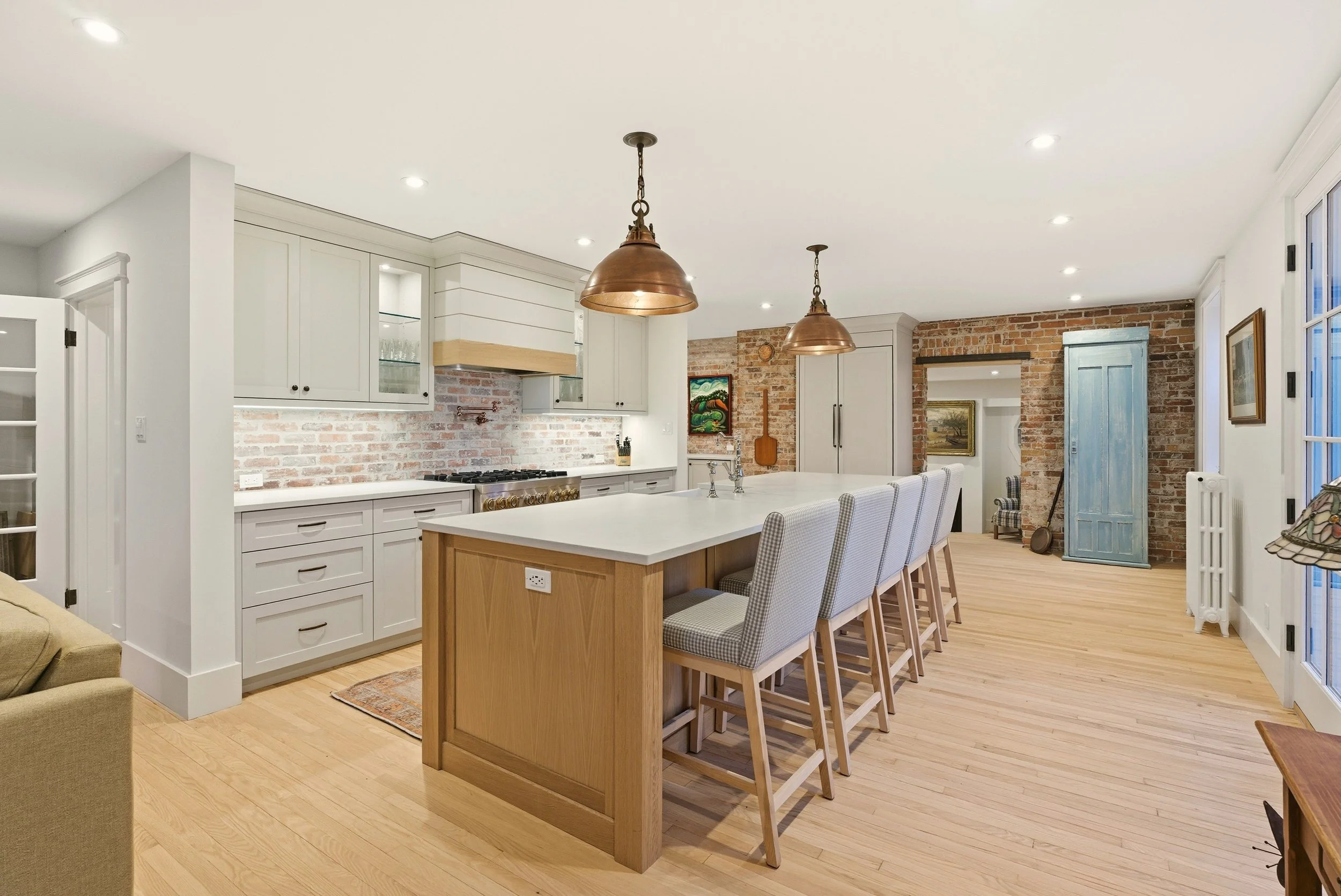 Modern kitchen with exposed brick walls, white cabinetry, a large island with four chairs, and pendant lighting.