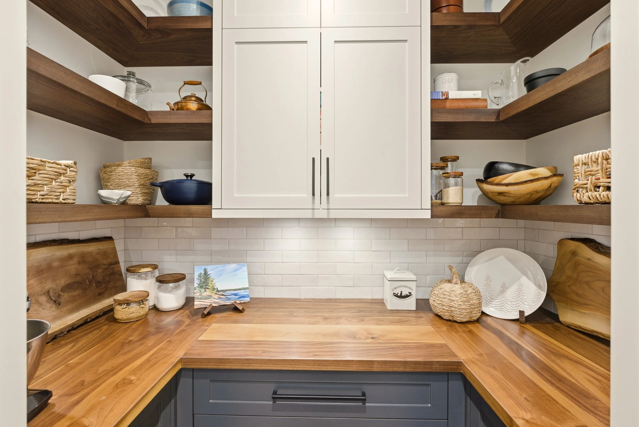 Kitchen with wooden countertops, white tile backsplash, open wooden shelves with kitchenware, and white upper cabinets.