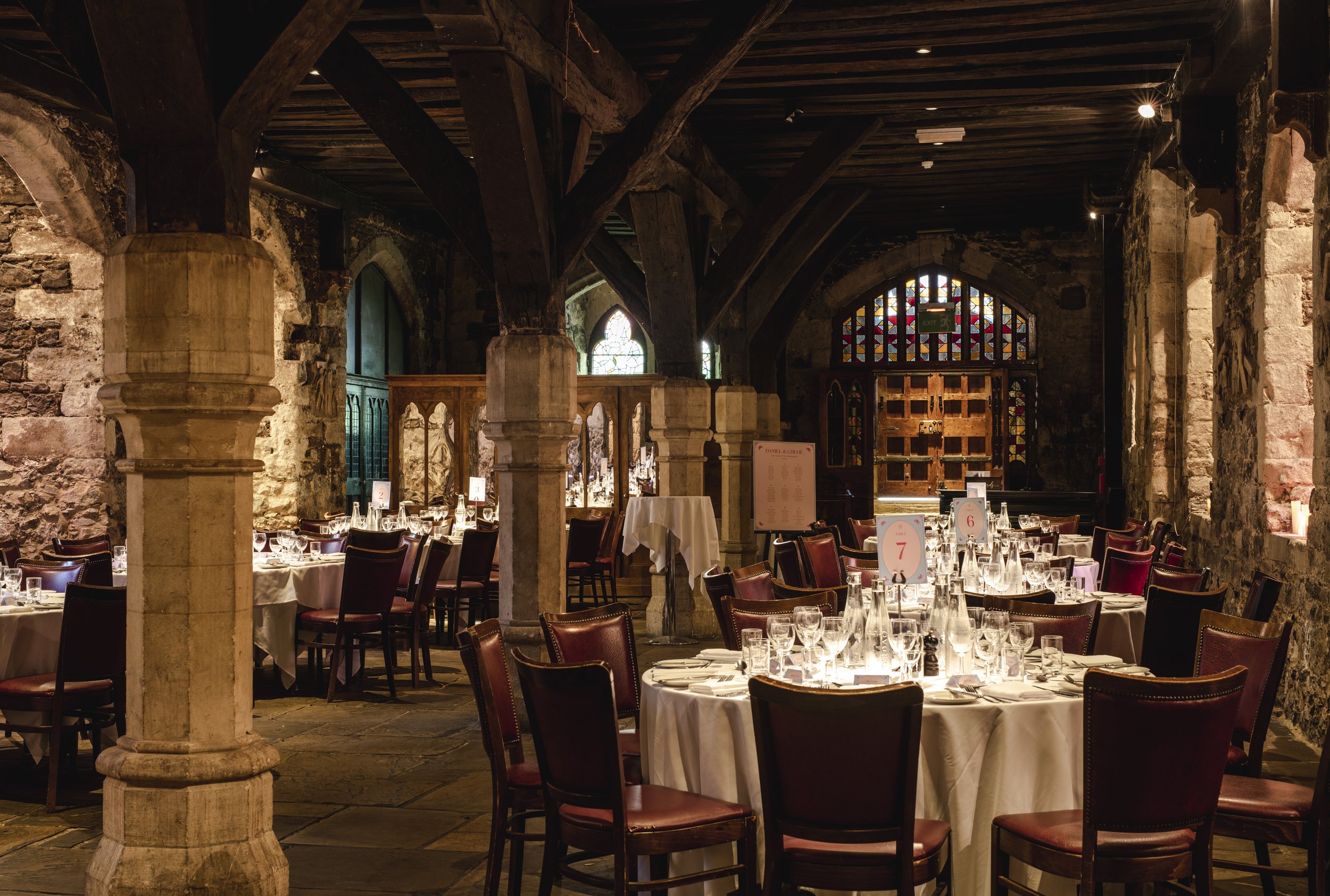 Interior of a historic stone-built restaurant or banquet hall with wooden beams, round tables with white tablecloths, and chairs set for a meal.