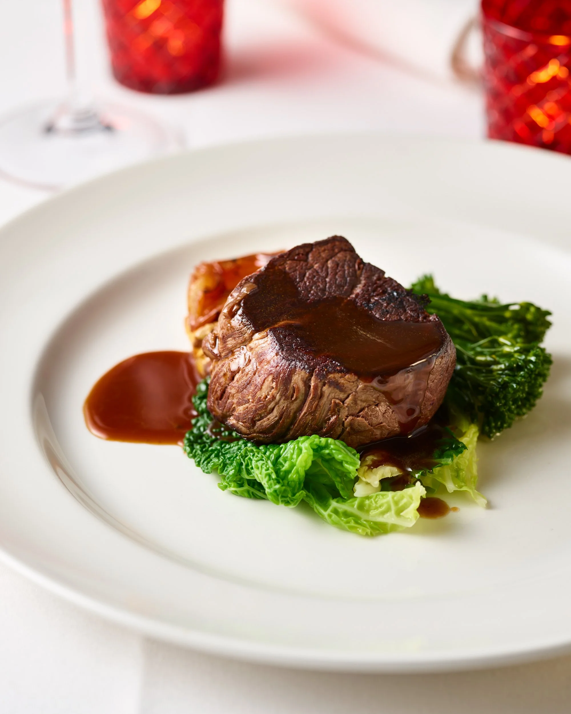 A plated beef steak topped with brown gravy, served with leafy green vegetables on a white plate.