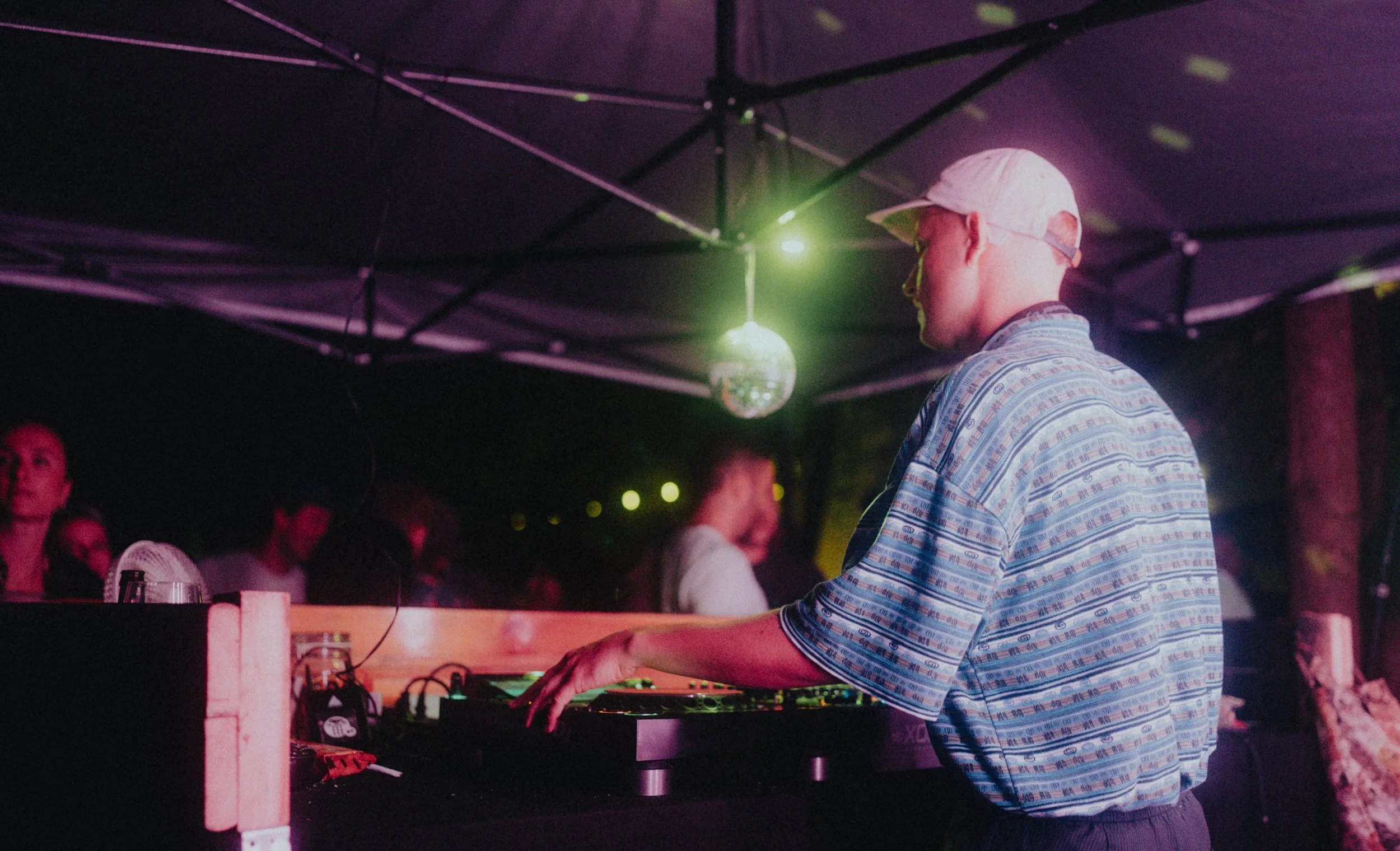 DJ spielt auf einer Party unter einem Zelt mit Disco-Kugel und Lichtprojektionen.