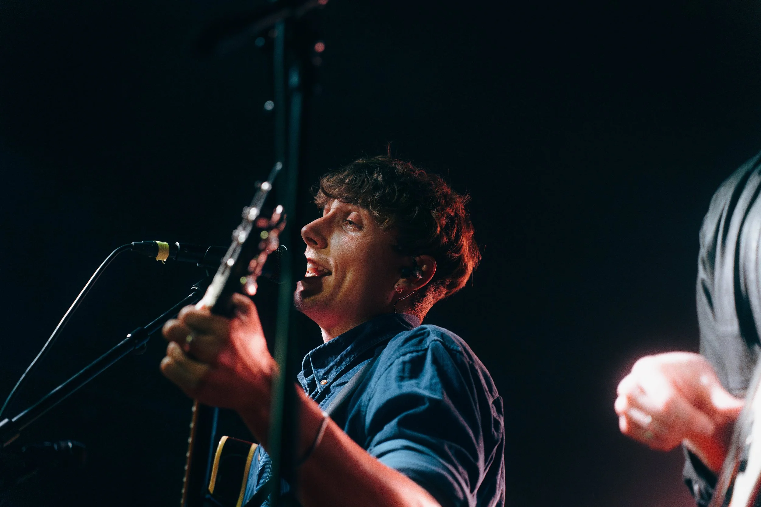 Junger Mann spielt Gitarre und singt in einem dunklen Raum bei einem Live-Auftritt.