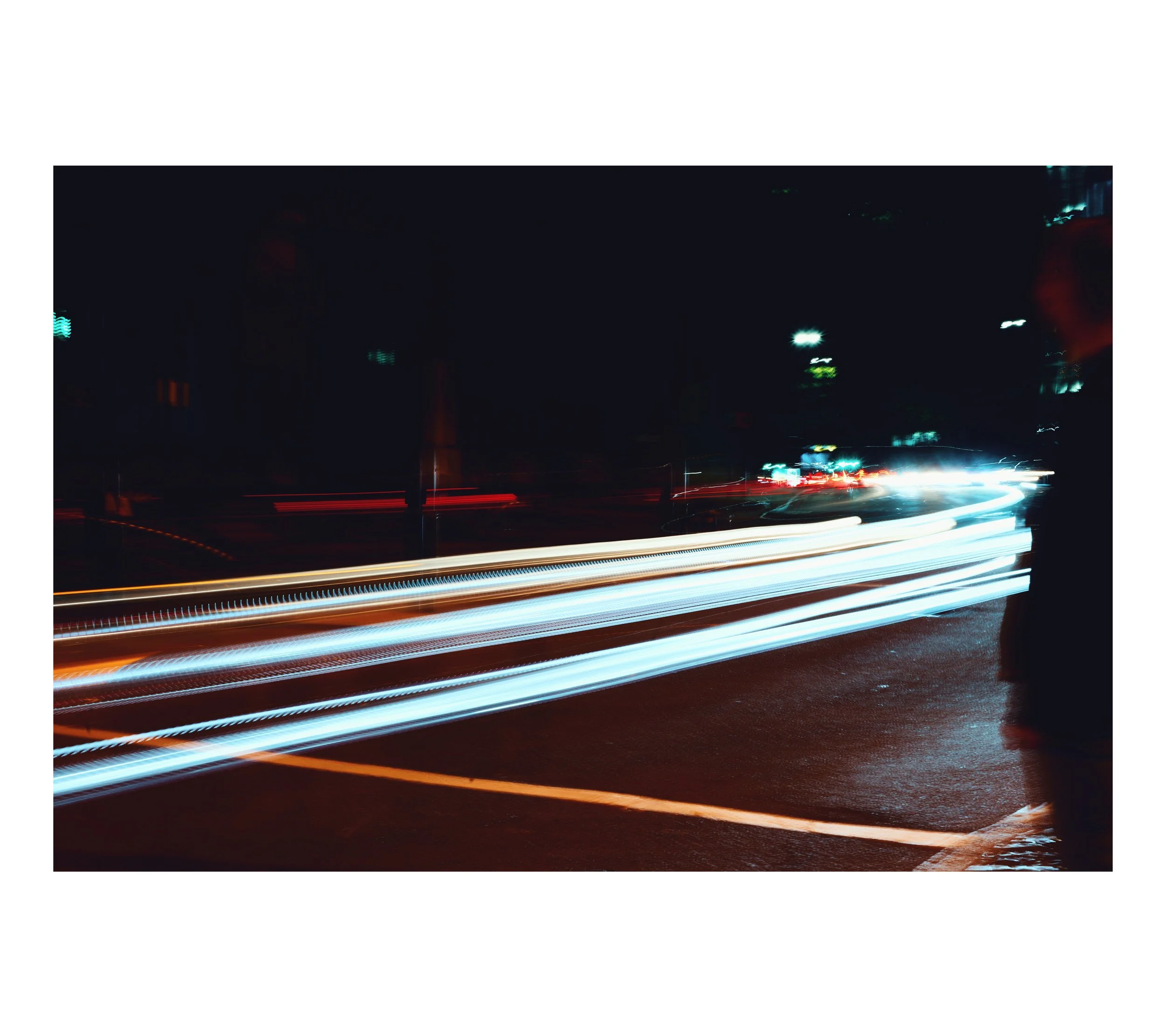 Nachtaufnahme mit Lichtspuren von fahrenden Autos auf einer Straße.