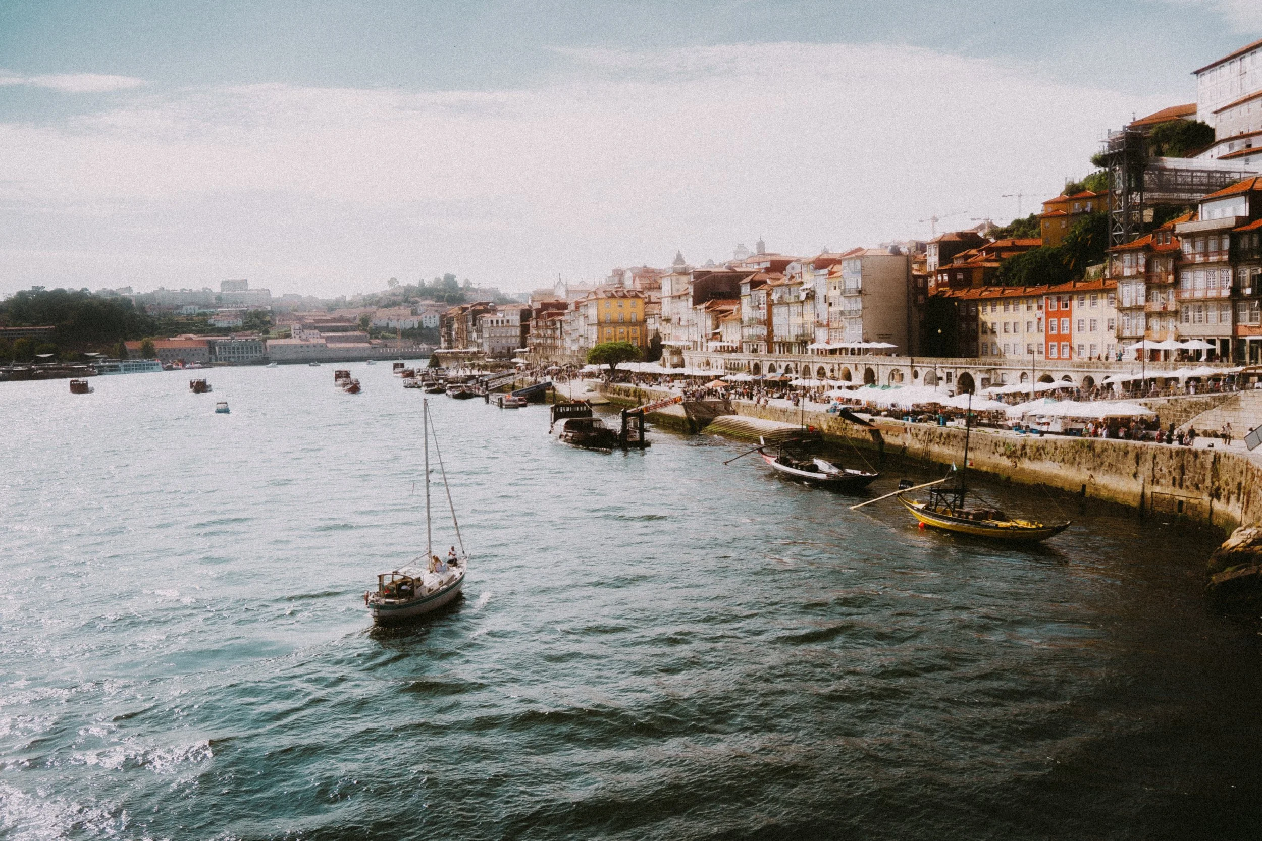 Blick auf eine Uferpromenade mit bunten Häusern und Segelbooten im Wasser.