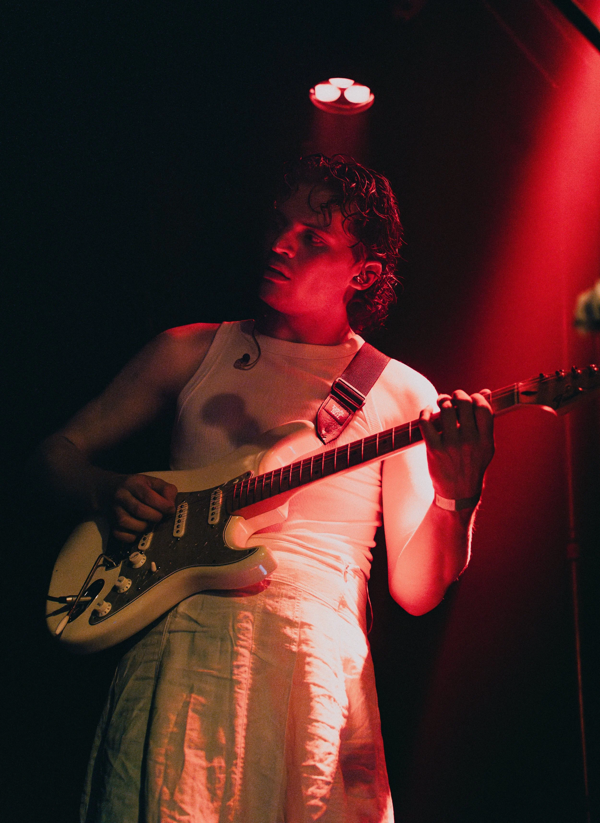 Musikerin spielt Gitarre auf Bühne bei rotem Licht.