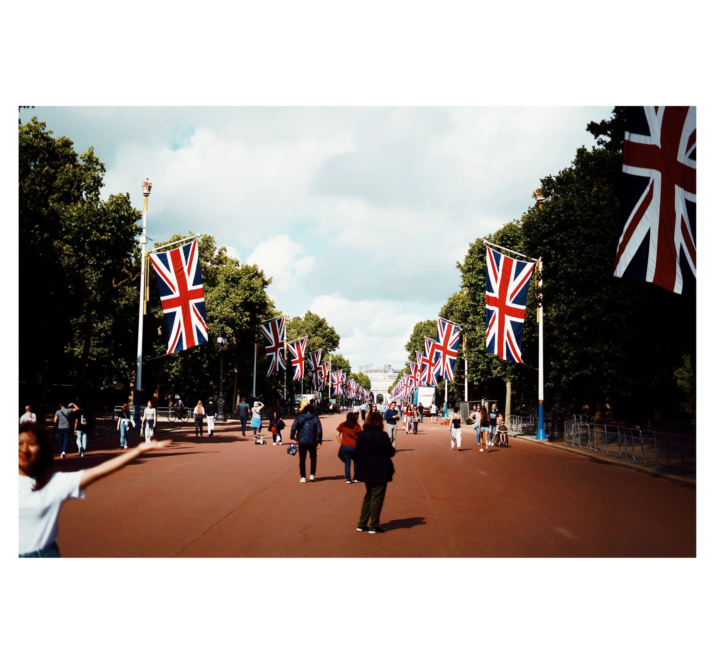 Menschen auf der Westminster Bridge in London, umgeben von britischen Flaggen, bei schönem Wetter mit Wolken am Himmel.