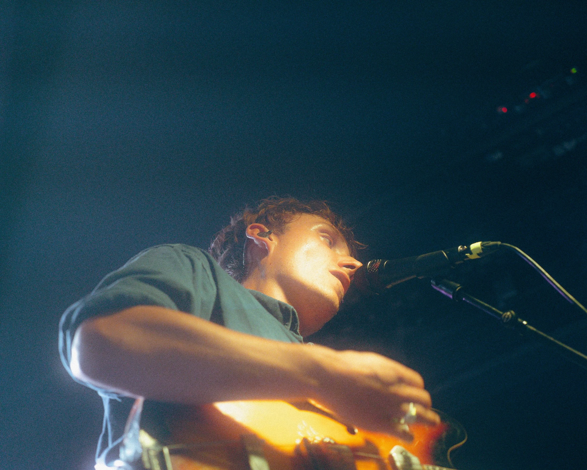 Ein junger Musiker singt in ein Mikrofon und spielt Gitarre auf der Bühne.