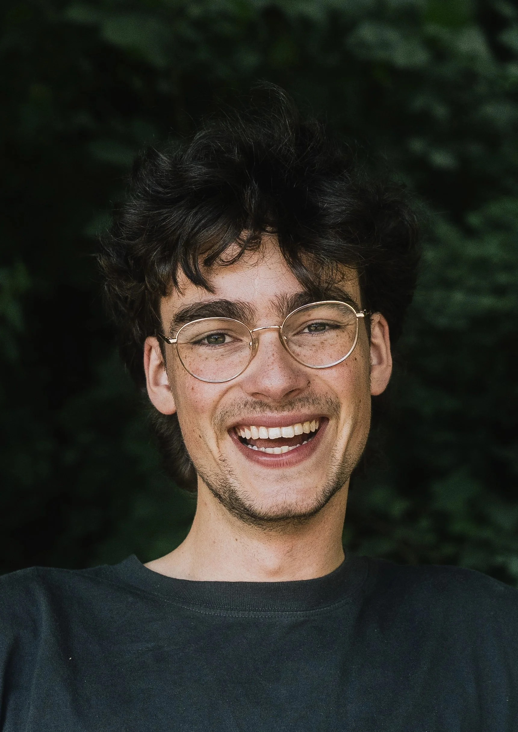 Ein lachender junger Mann mit Brille vor einem grünen Hintergrund.