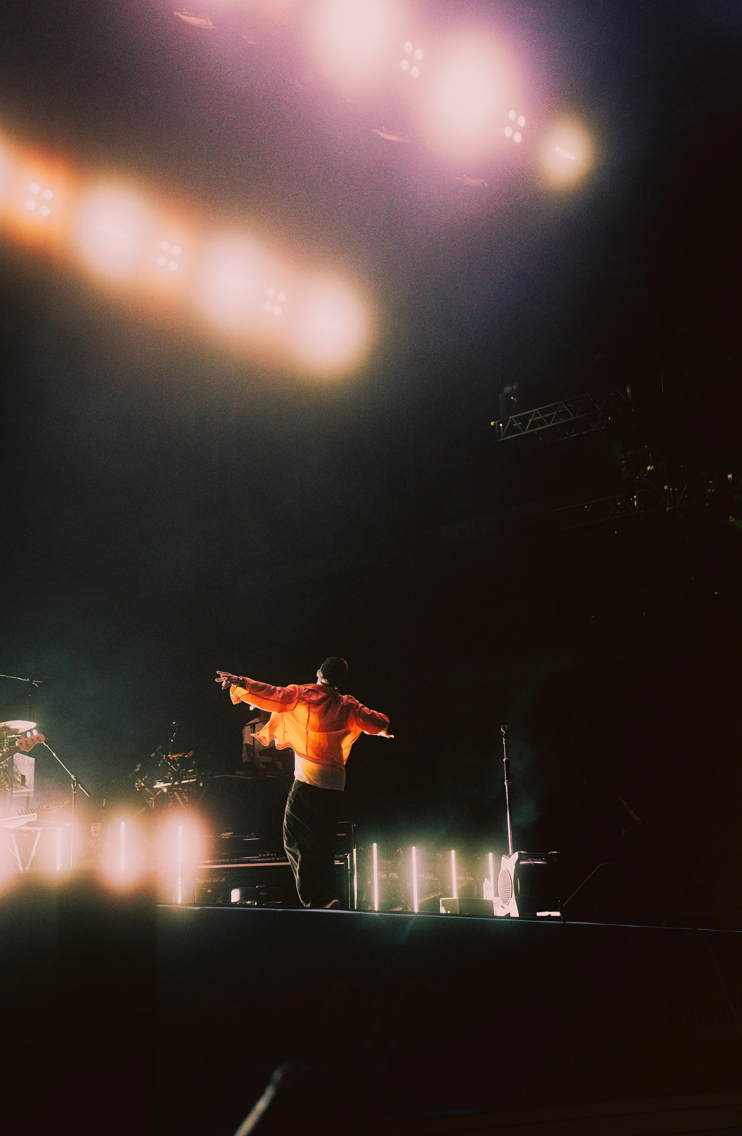 Künstler auf der Bühne bei einem Konzert im Scheinwerferlicht, mit Musikern und Bühnenausstattung im Hintergrund.