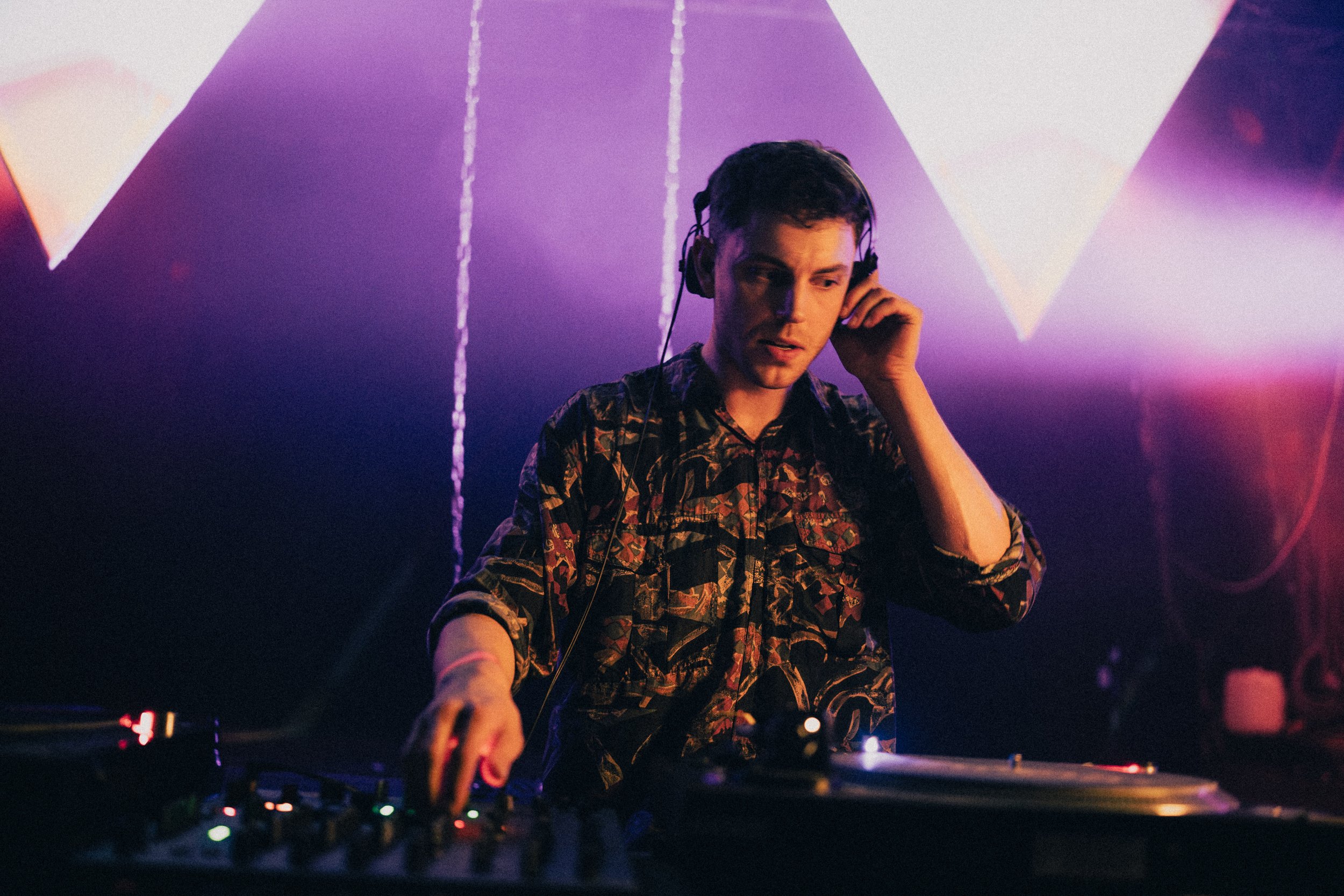 DJ mit Kopfhörern am Pult in einem dunklen, bunten Club mit Neon-Lichtspielen.