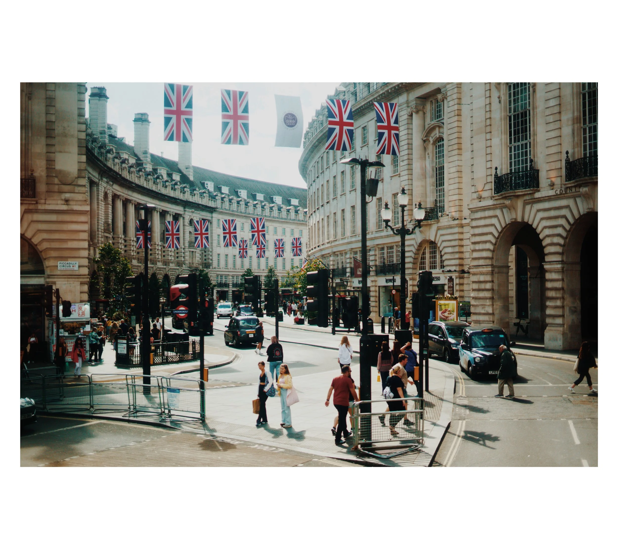 Straßenszene in London mit Menschen, Autos, Gebäude im neoklassizistischen Stil und britischen Flaggen.