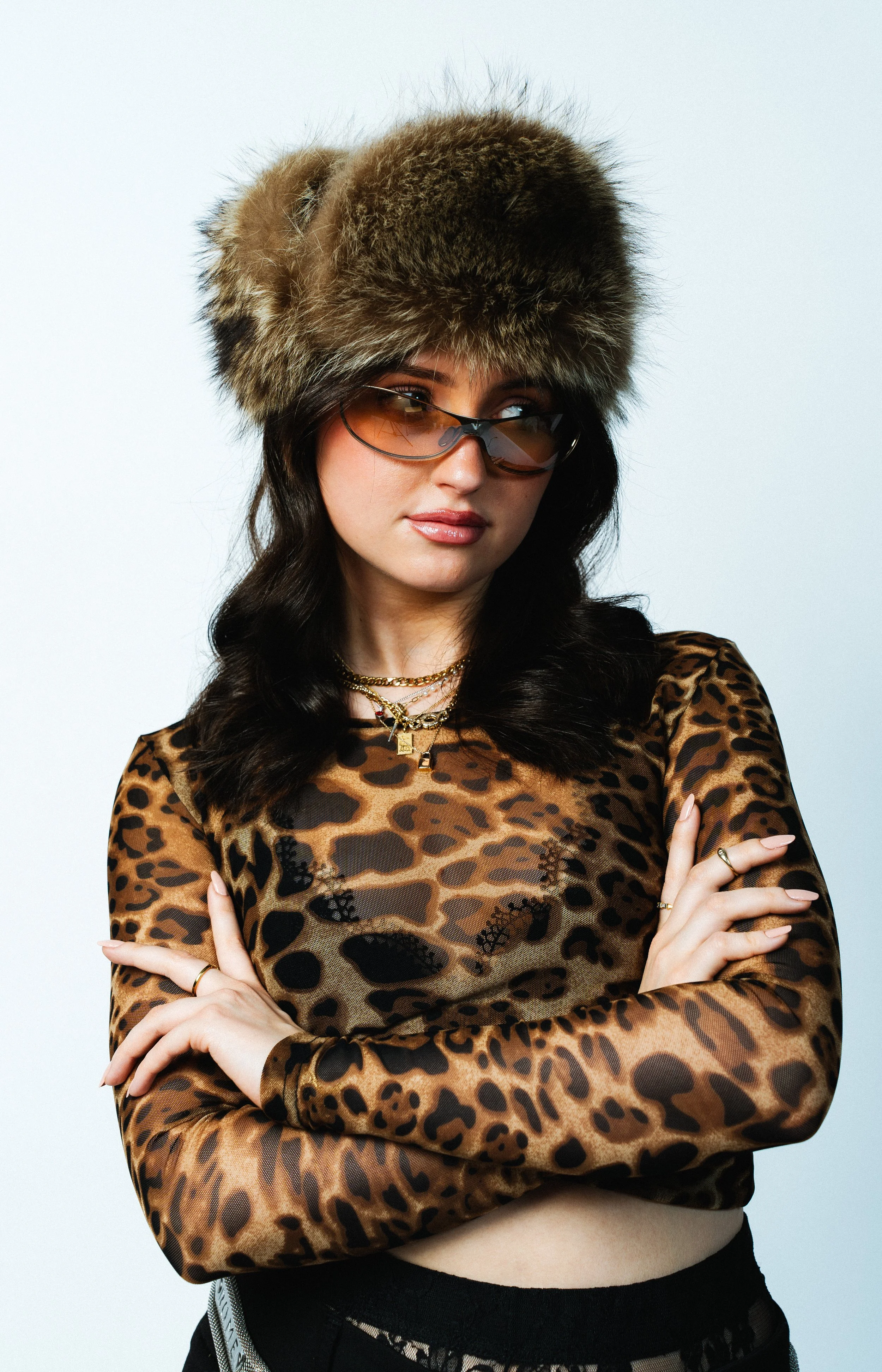 Junge Frau trägt einen Leoparden-Muster-Top, eine pelzbesetzte Mütze, Sonnenbrille und Schmuck.