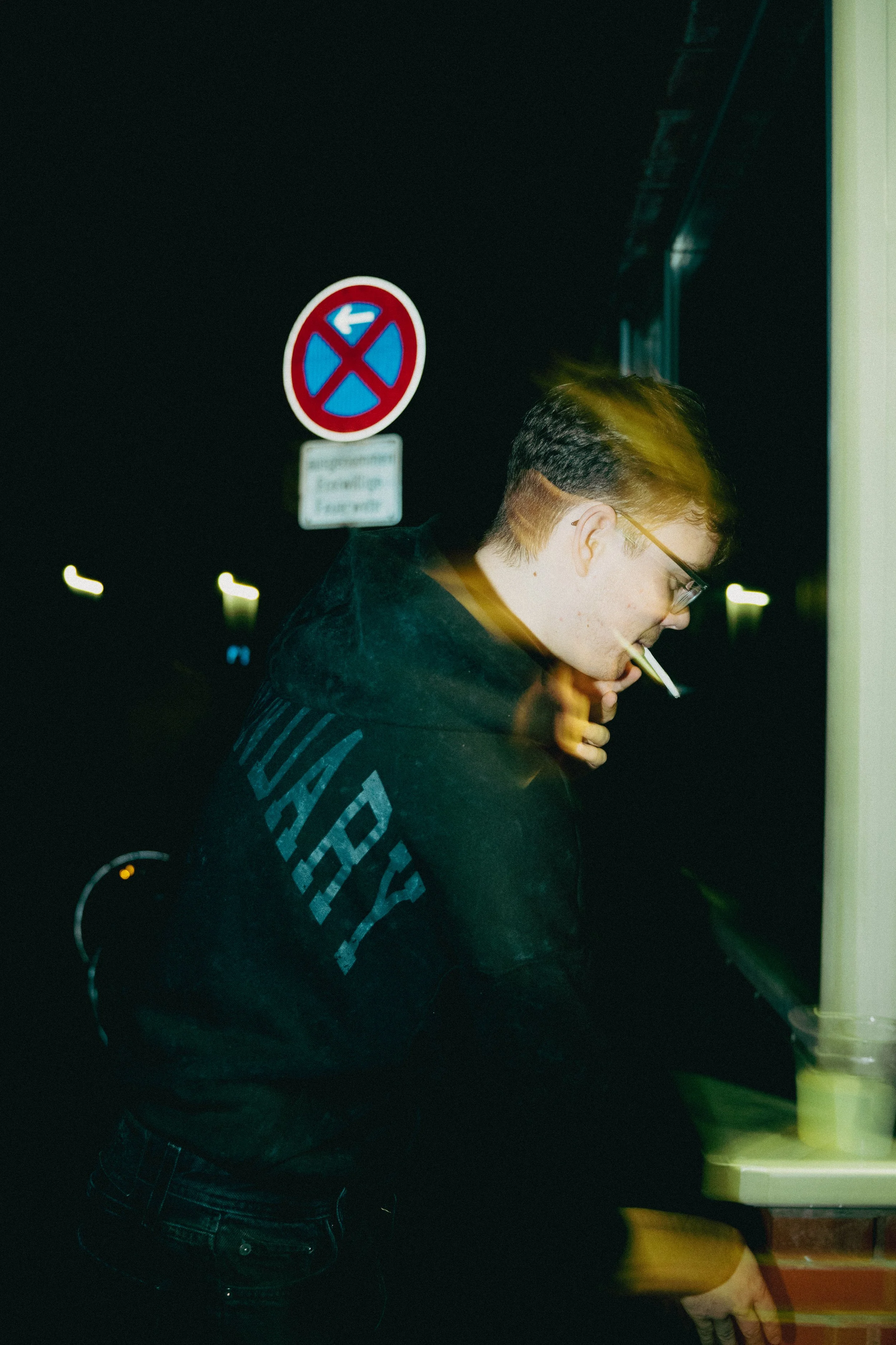 Mann mit Brille und Zigaretten im Mund steht an einem dunklen Abend an einem Verkaufsstand.