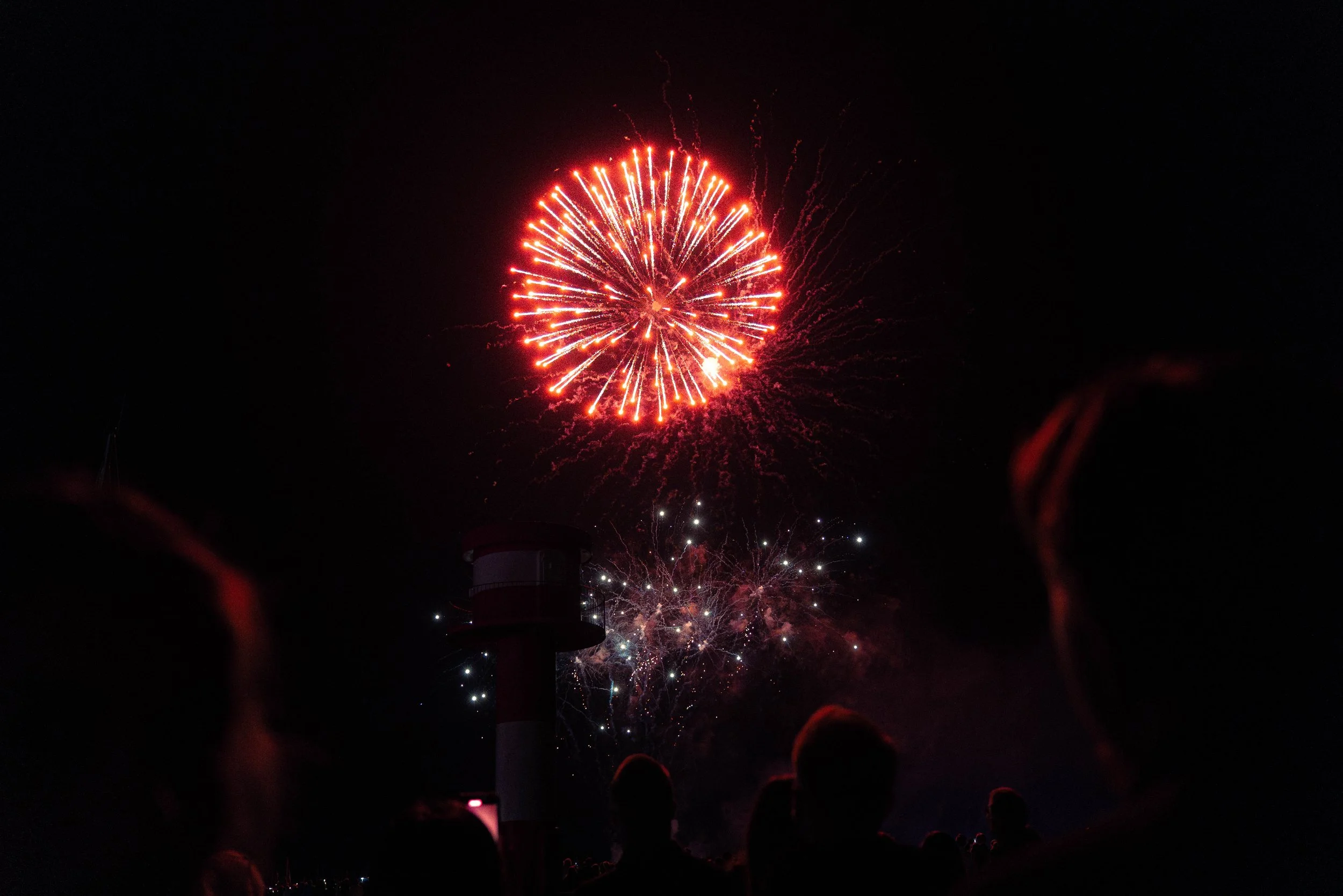 Feuerwerk erleuchtet den Nachthimmel während eines Festivals, mit Menschen im Vordergrund, die das Spektakel beobachten.