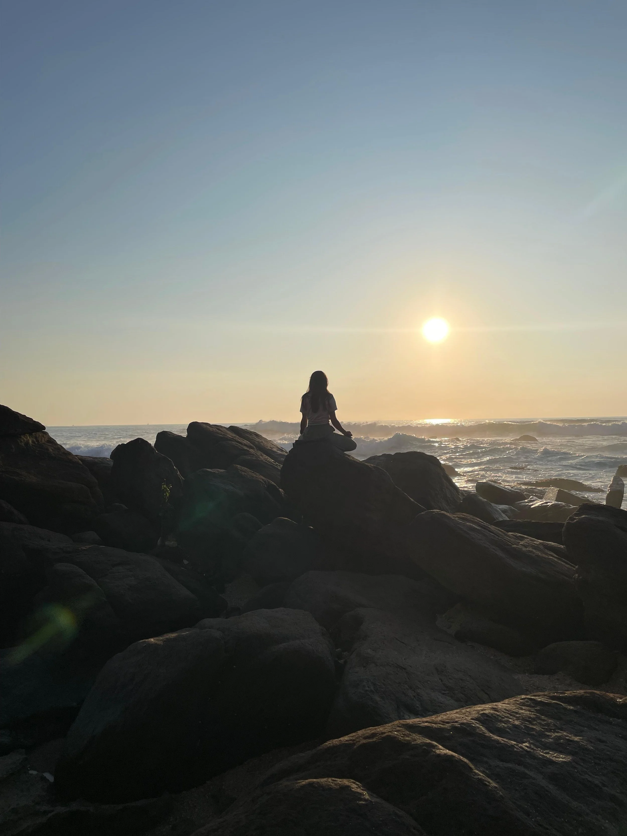 Eine Person sitzt im Lotussitz auf Felsen am Strand während des Sonnenuntergangs, Blick auf das Meer. Meditation, Sri Lanka