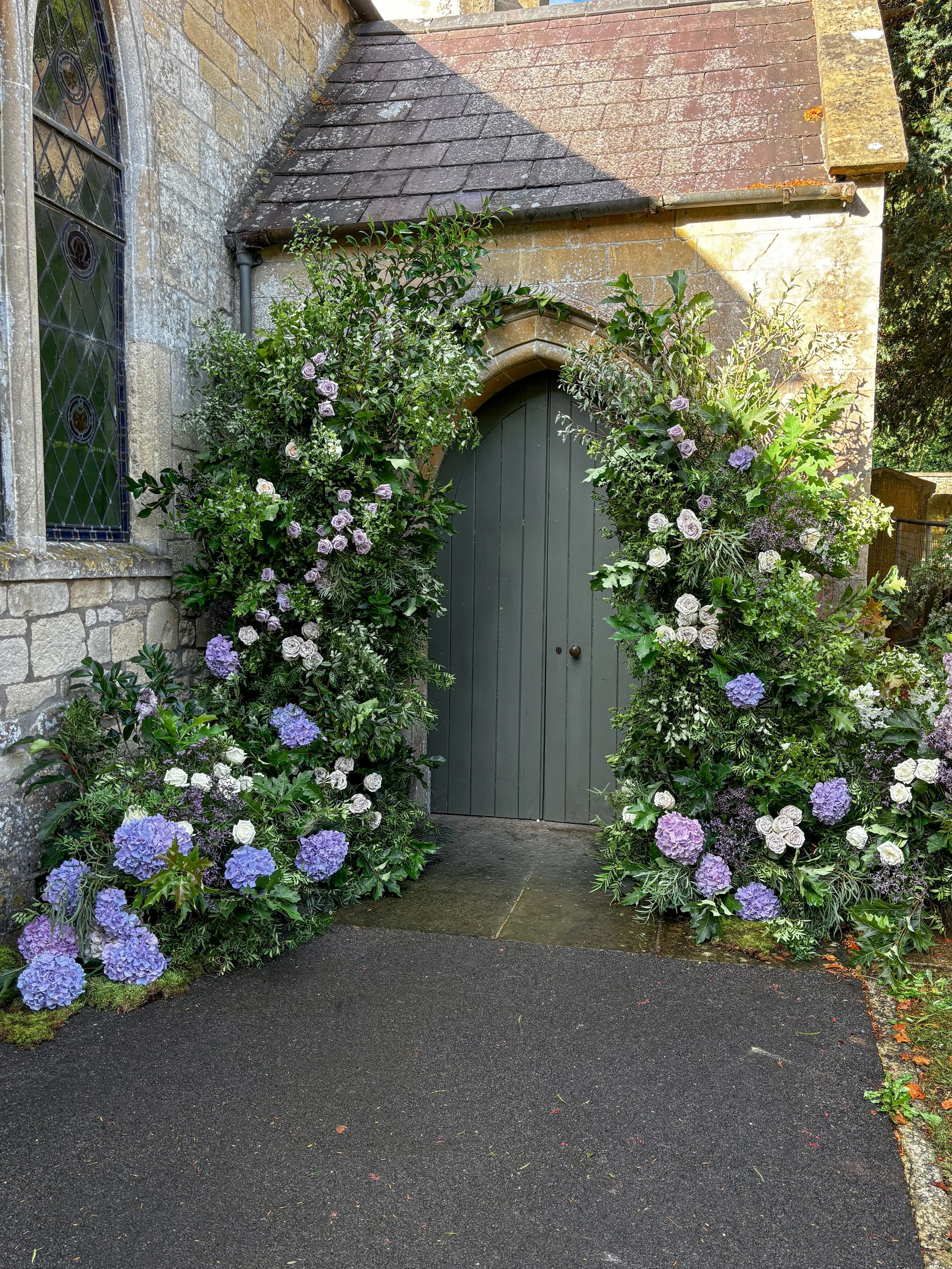Floral arch for a church wedding ceremony in Combe Hay, Somerset, featuring white and green flowers with soft lilac tones.