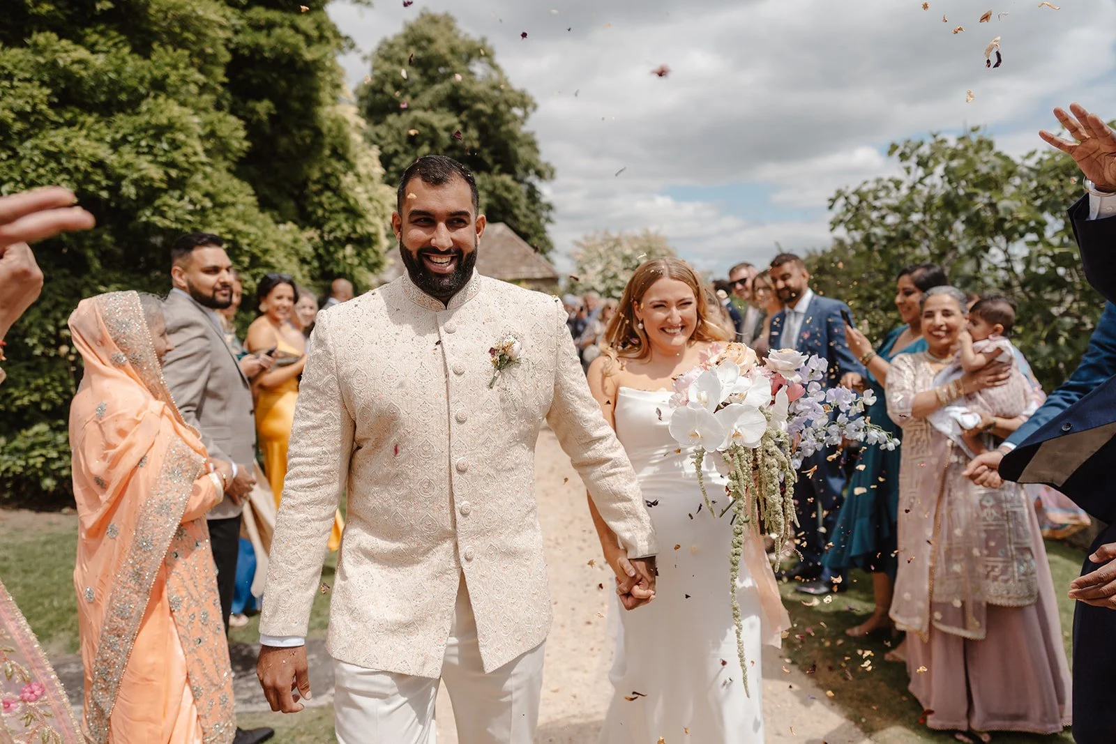 Joyful Indian wedding confetti exit at Hamswell House with cascading white orchid bridal bouquet
