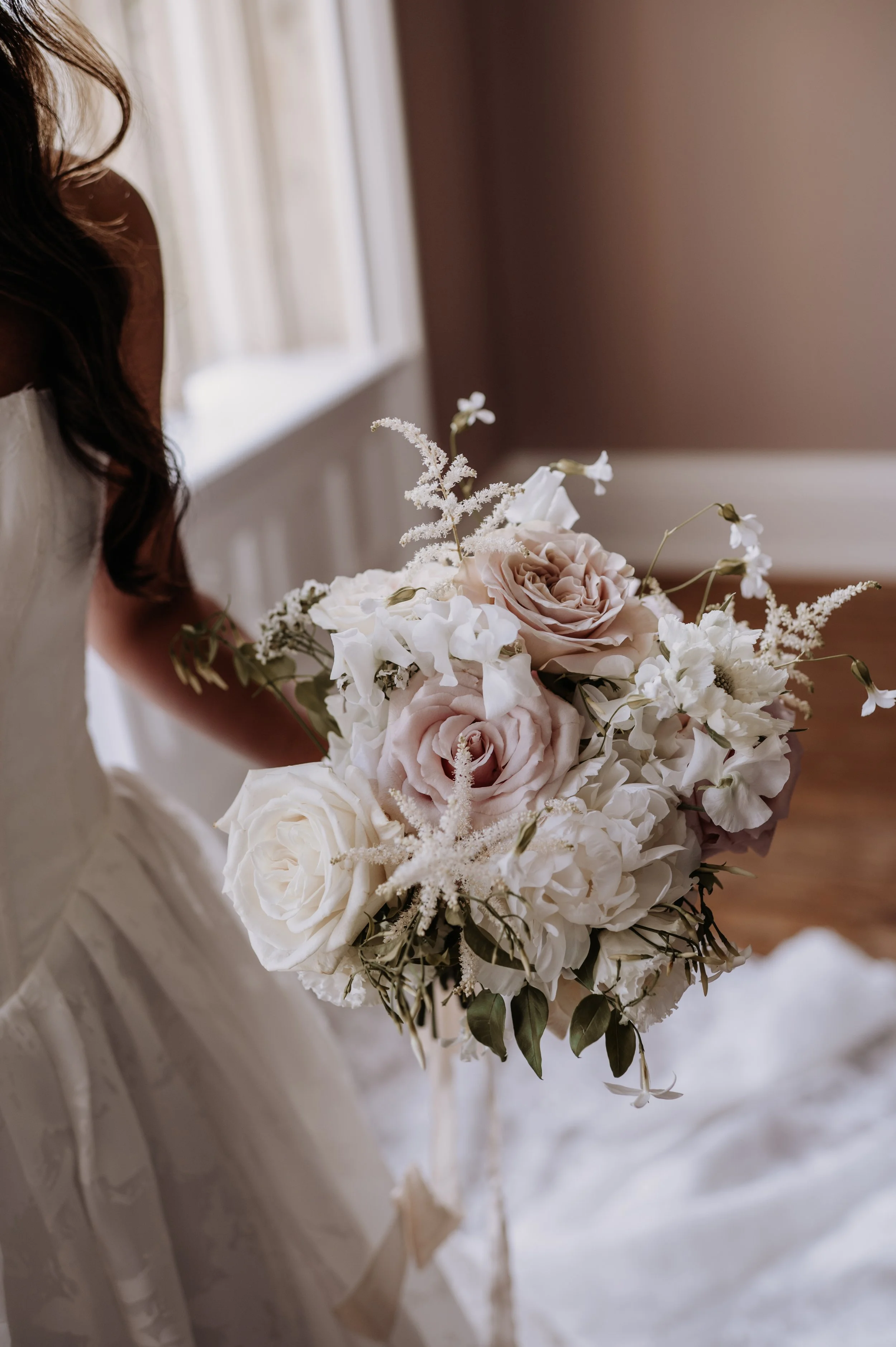 Bridal bouquet of white and soft blush roses, peonies, astilbe and trailing jasmine vines.
