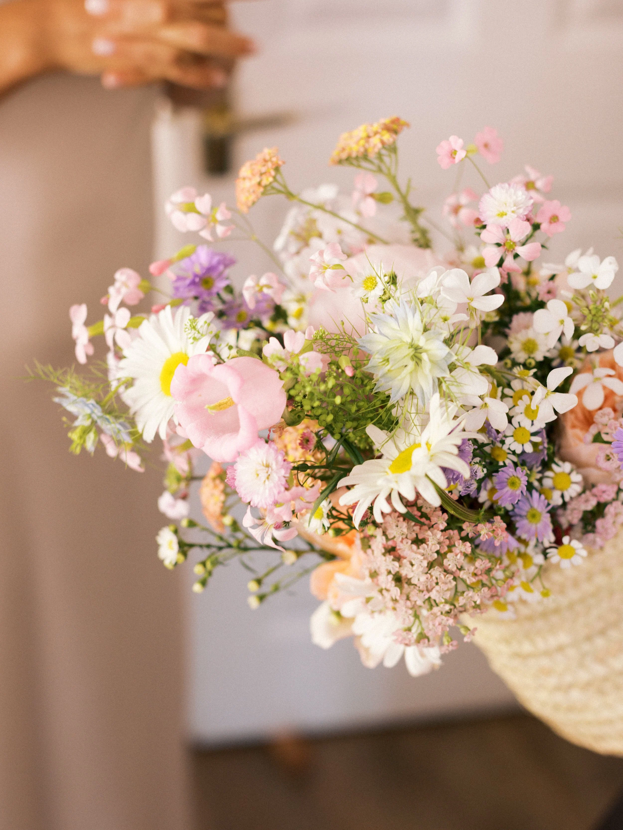 Close-up of a bridal basket arrangement with asters, daisies, campanula, peony, sweet rocket and garden roses for a spring wedding.
