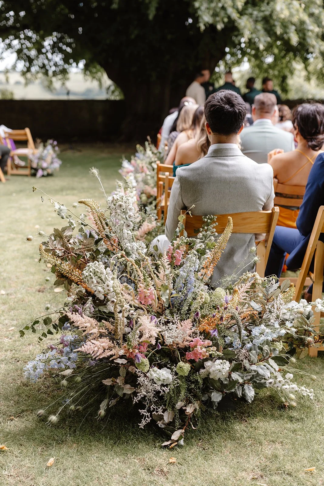 Large floral meadow installation marking the entrance to the ceremony aisle at Hamswell House, Bath, created for a June wedding beneath the historic lime tree. Designed in a natural garden style with Astilbe, Stocks, Delphinium, Eremurus, Clematis an