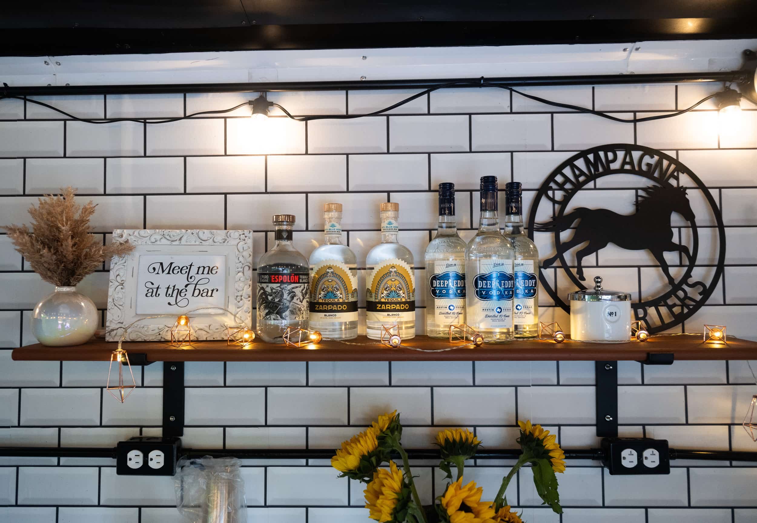 Champagne Quarters horse trailer mobile bar - the image provides a sneak-peek of the backsplash of horse trailer, the shelf lined with liquor bottles and fun decor.