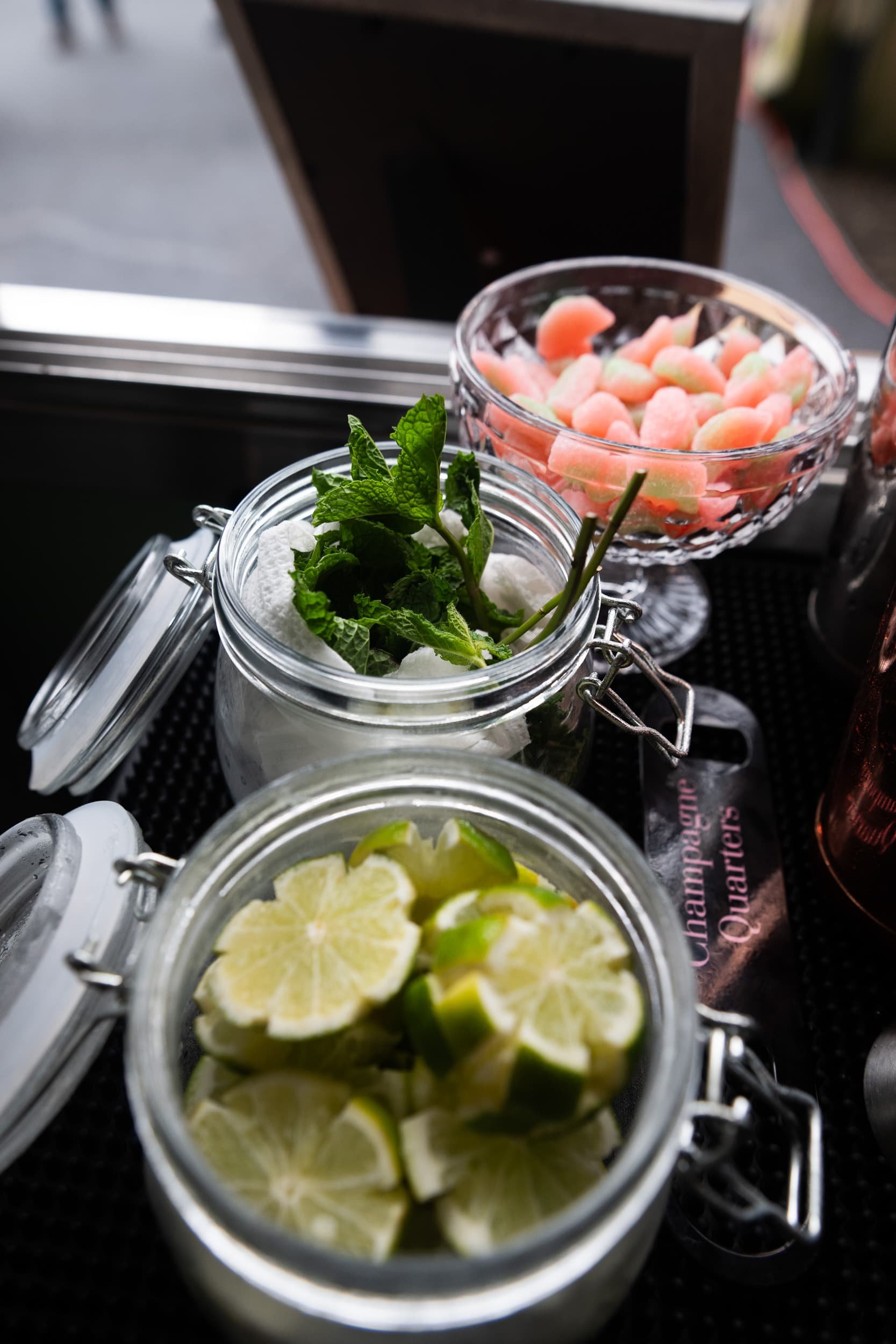 Champagne Quarters mobile bar serving cocktails and closeup of garnishes including lime cut into a flower, mint, and some sour watermelon candy for the signature drinks.