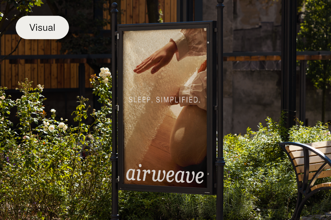 Outdoor advertising board with an image of a hand reaching over a bed, and the words 'Sleep, Simplified.' and 'airweave' in white text, with greenery and a bench nearby.