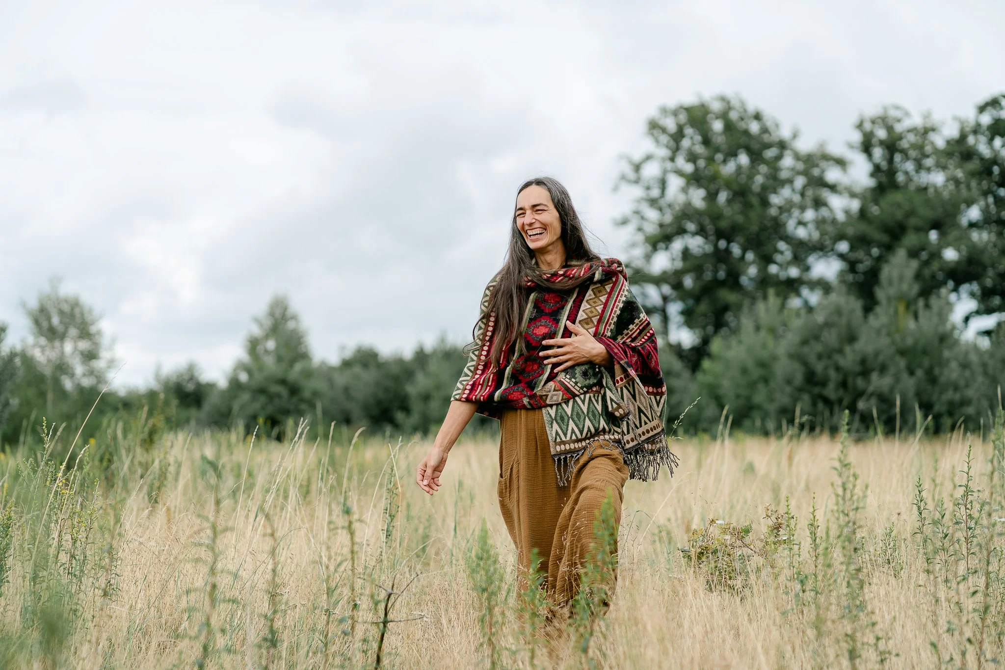 Smiling woman in a colourful shawl walking through a dry grass meadow