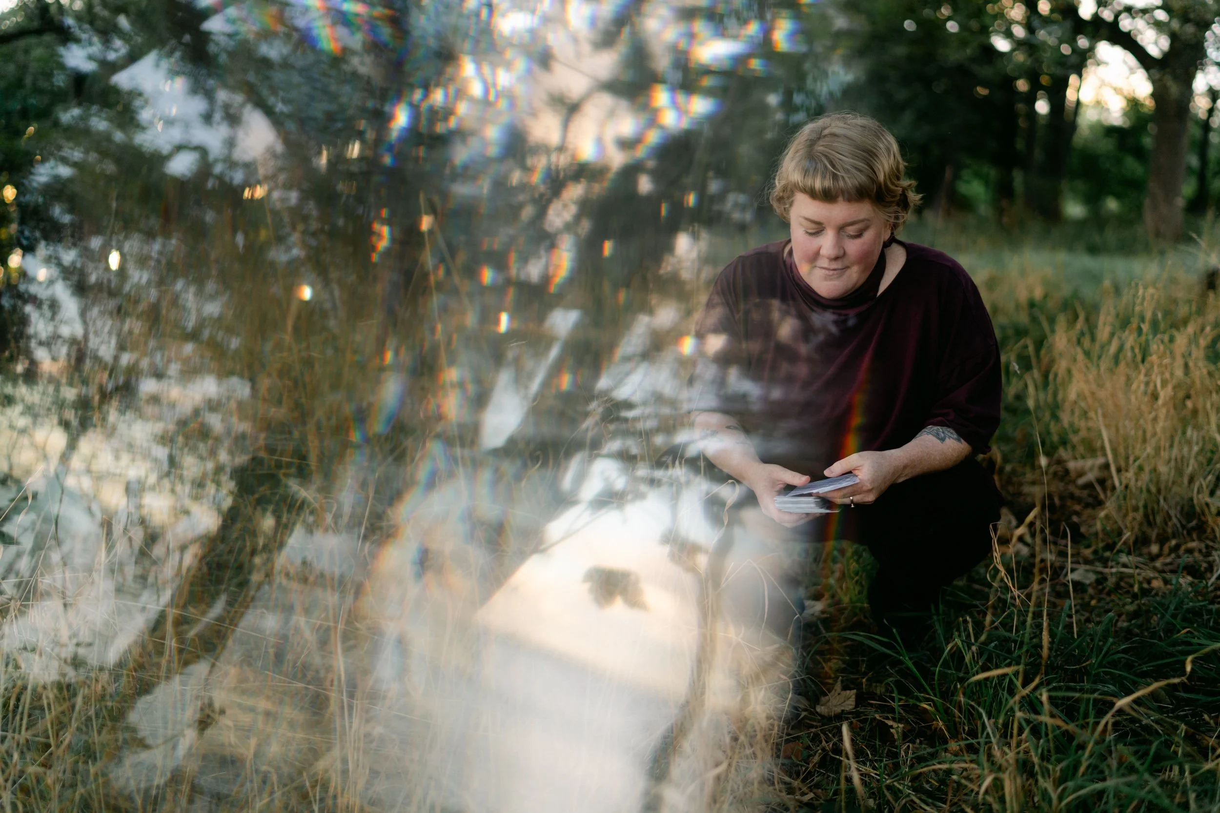 female business owner sitting in a park with tarot cards, prism reflects trees
