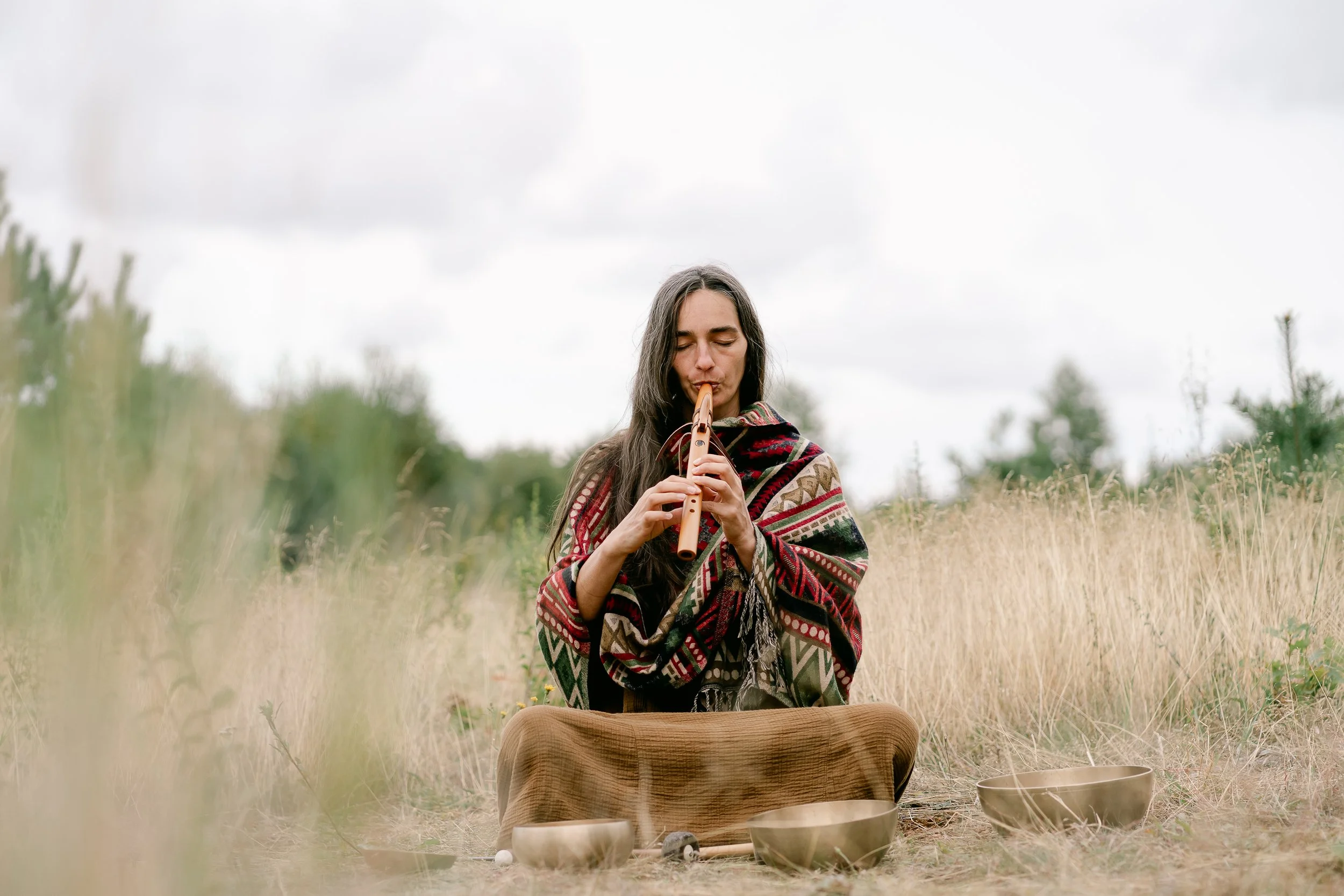 sound healer photographed playing flute in an open field