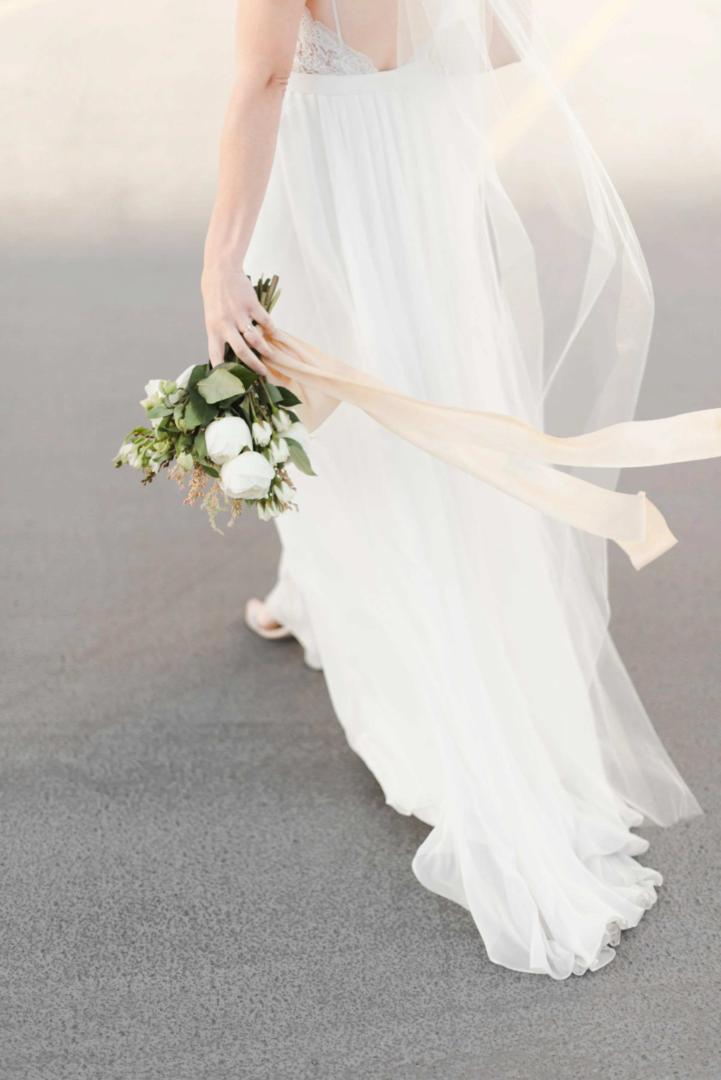 Bride in a flowing white wedding dress holding a bouquet of white roses and greenery on a gray surface at Timeless Tree Studios, the best photography studio in Toronto.