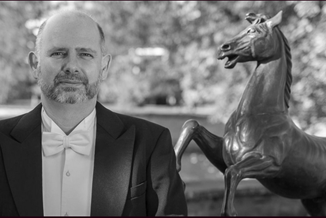 Ein Mann sthet vor einer Pferdestatue und schaut in die Kamera.