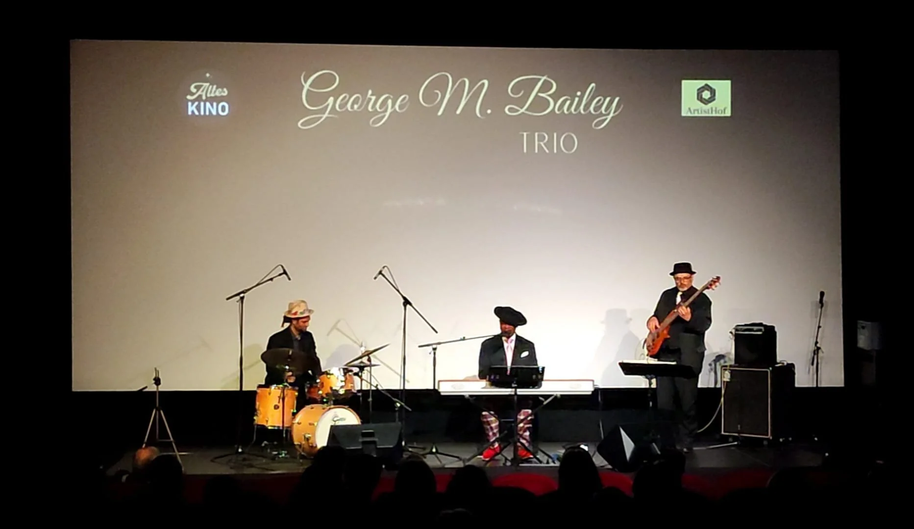 Drei Musiker stehen auf einer Bühne und spielen Instrumente