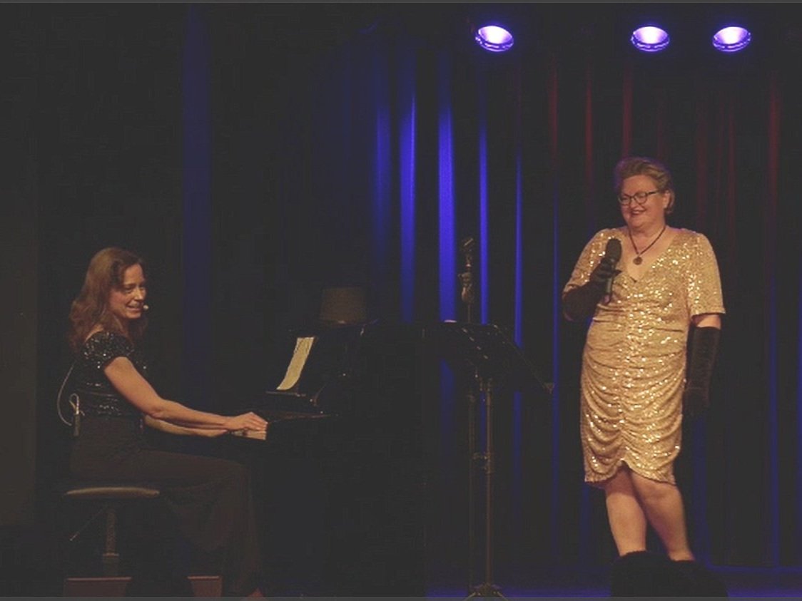 Zwei Musikerinnen stehen auf der Bühne vor einem blauen Vorhang