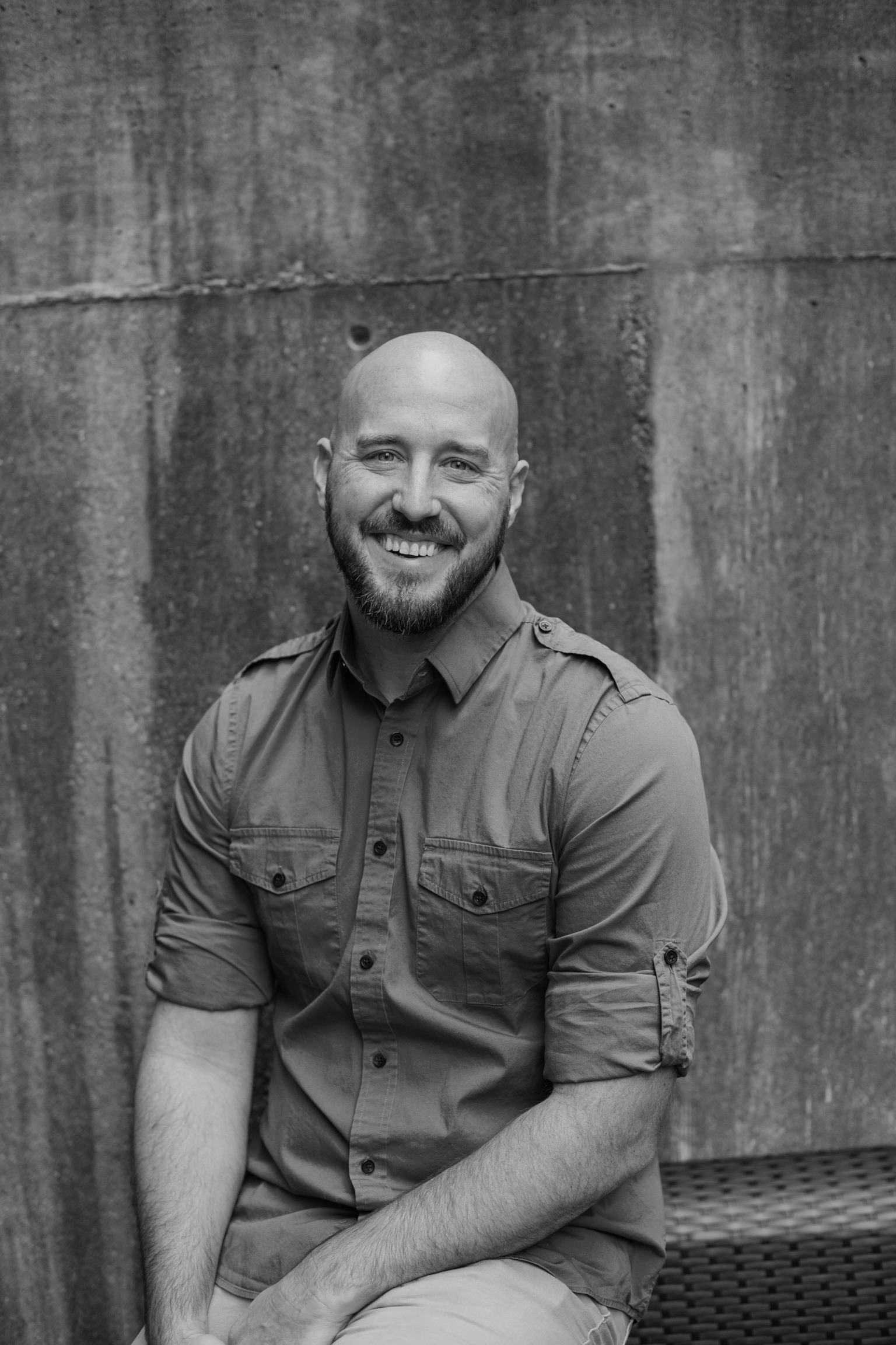 Black and white photo of Daniel smiling, sitting on concrete stairs outside, one with a beard in a dark shirt, and the other with long hair in a white shirt, both in casual jeans, black and white.