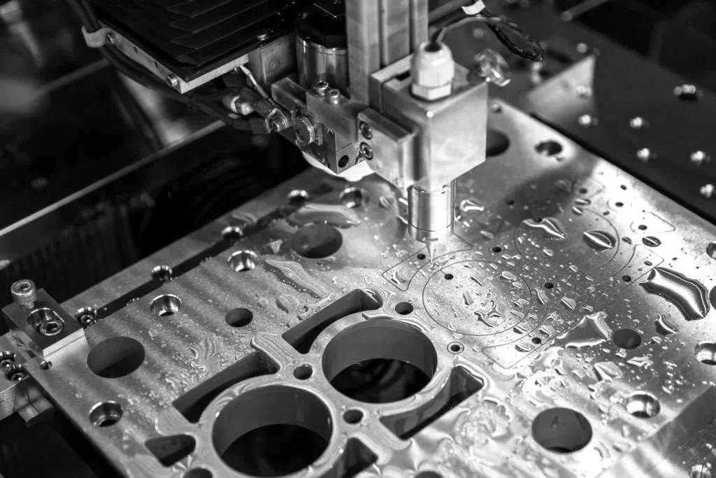 Close-up of a precision CNC machine drilling into a metal engine block with water cooling spray.