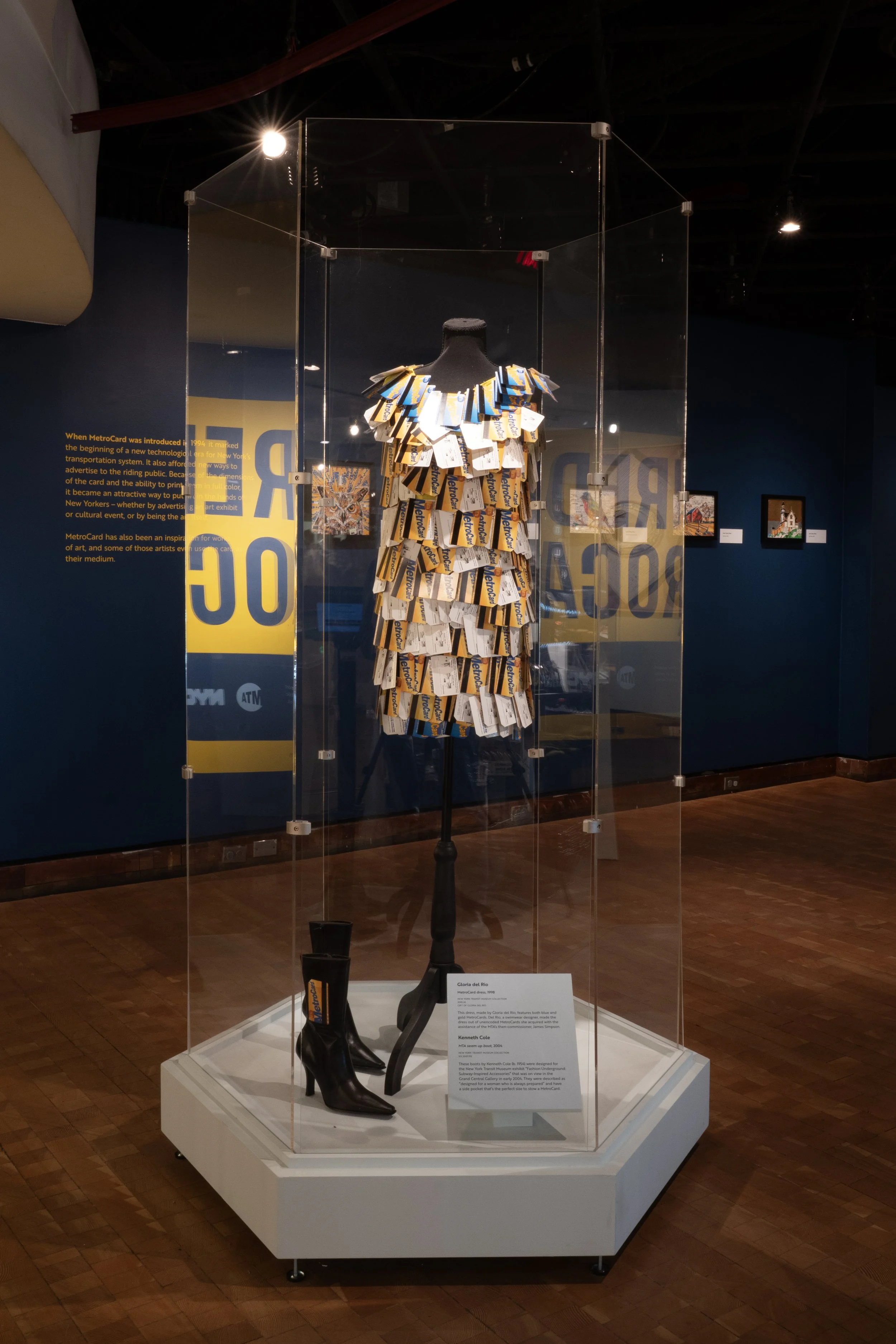 Custom hexagonal case containing a dress made of MetroCards by Gloria del Rio and a Kenneth Cole MetroCard boots
