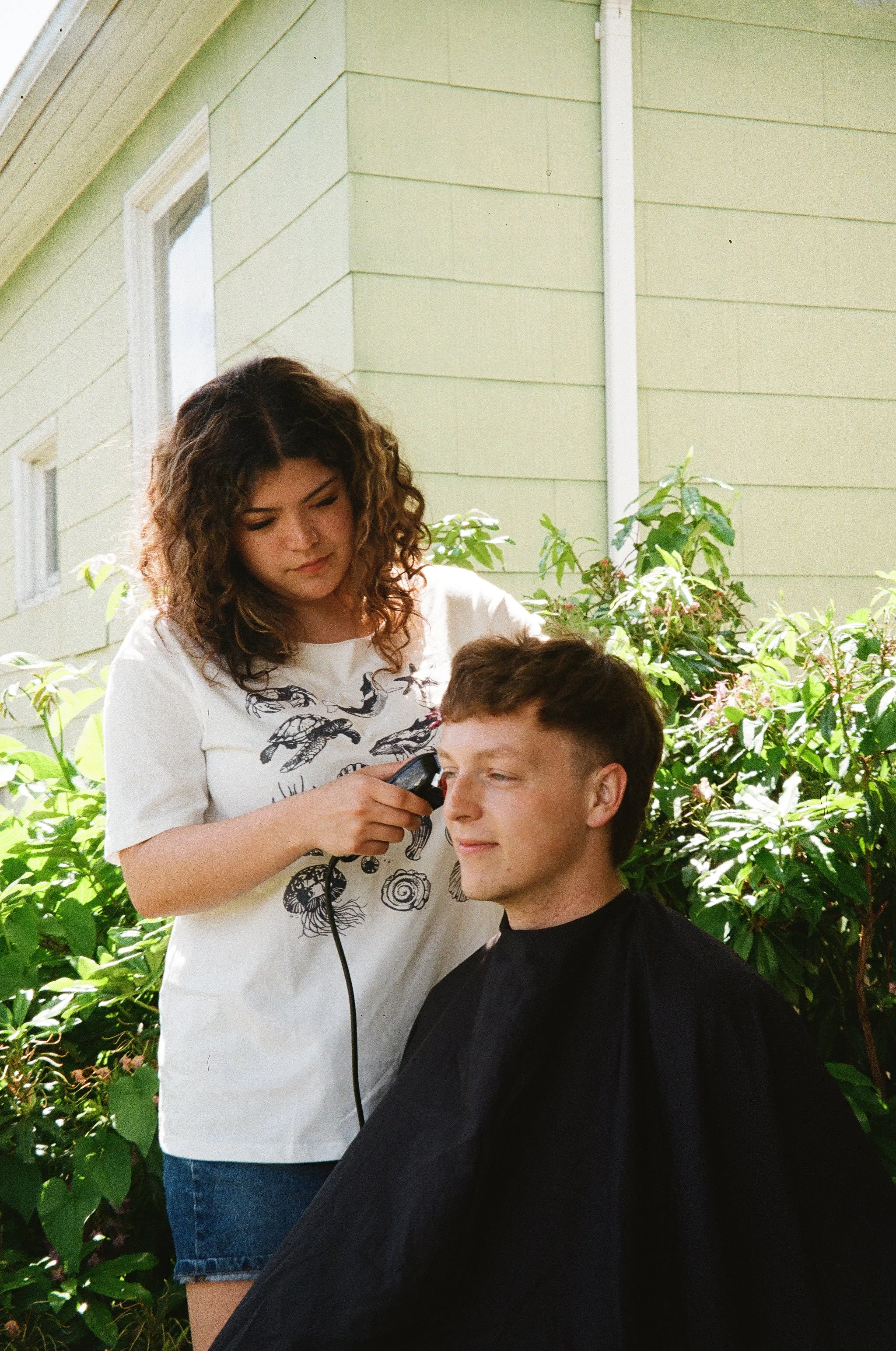 Kaleb Nichols gets a haircut by his roommate and hairdresser Emmaline Almacen on the front porch of their house in Bellingham, Wash.