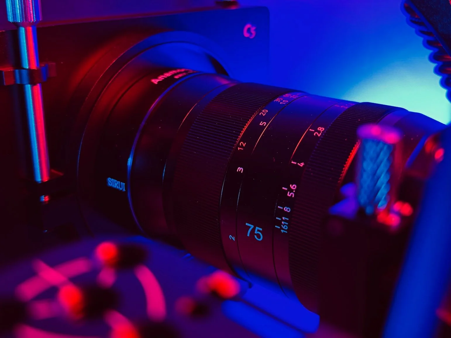 Close-up of a professional camera lens on a camera, illuminated by vibrant red and blue lighting.