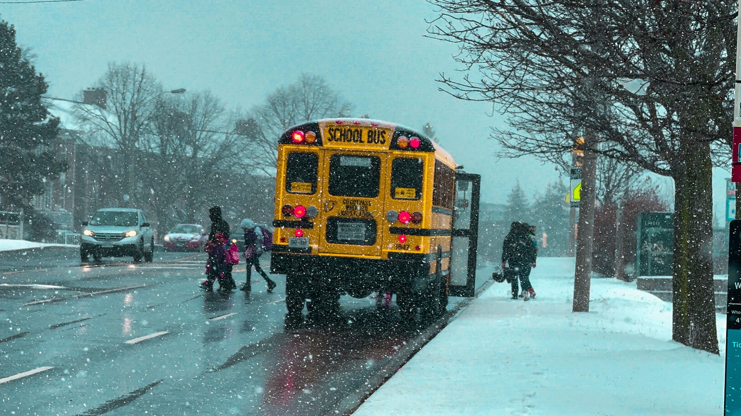 A family crossing the road from the school bus during a snow storm.