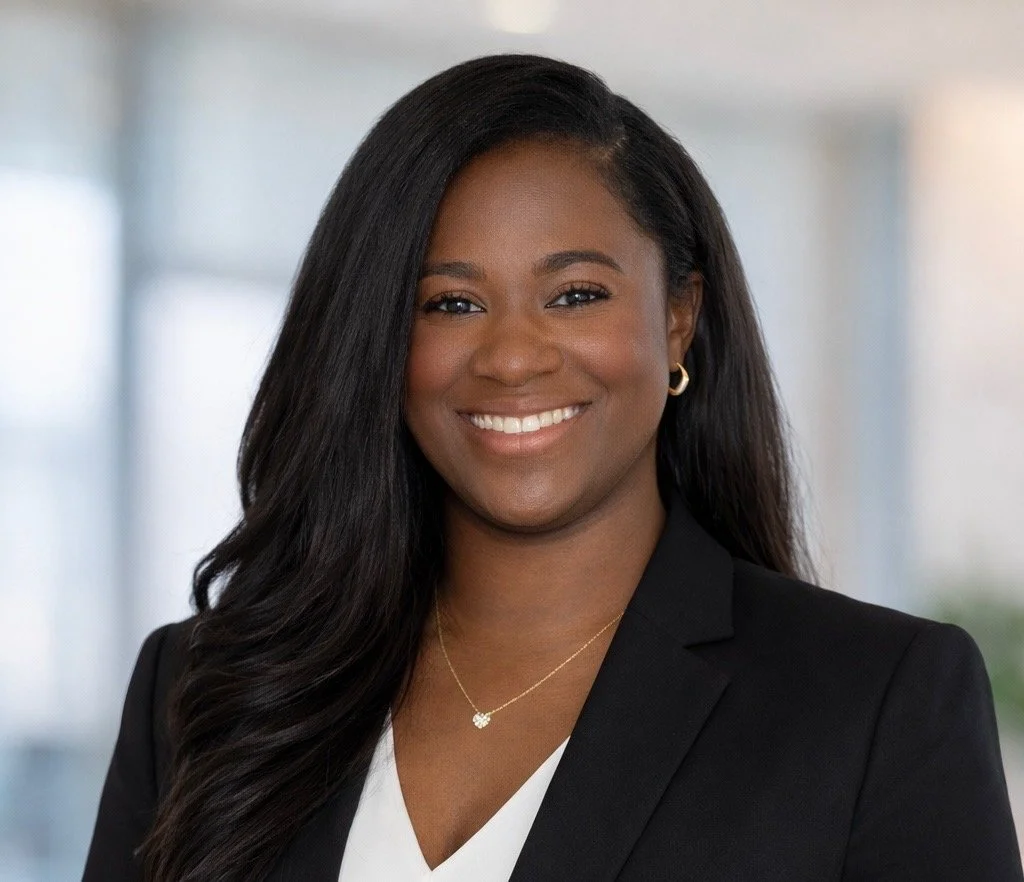 Professional portrait of a smiling African American woman with long black hair, wearing a black blazer, white top, and gold jewelry, in an indoor office setting. Speech therapy, speech therapist, pediatric speech therapy, speech language pathologist.