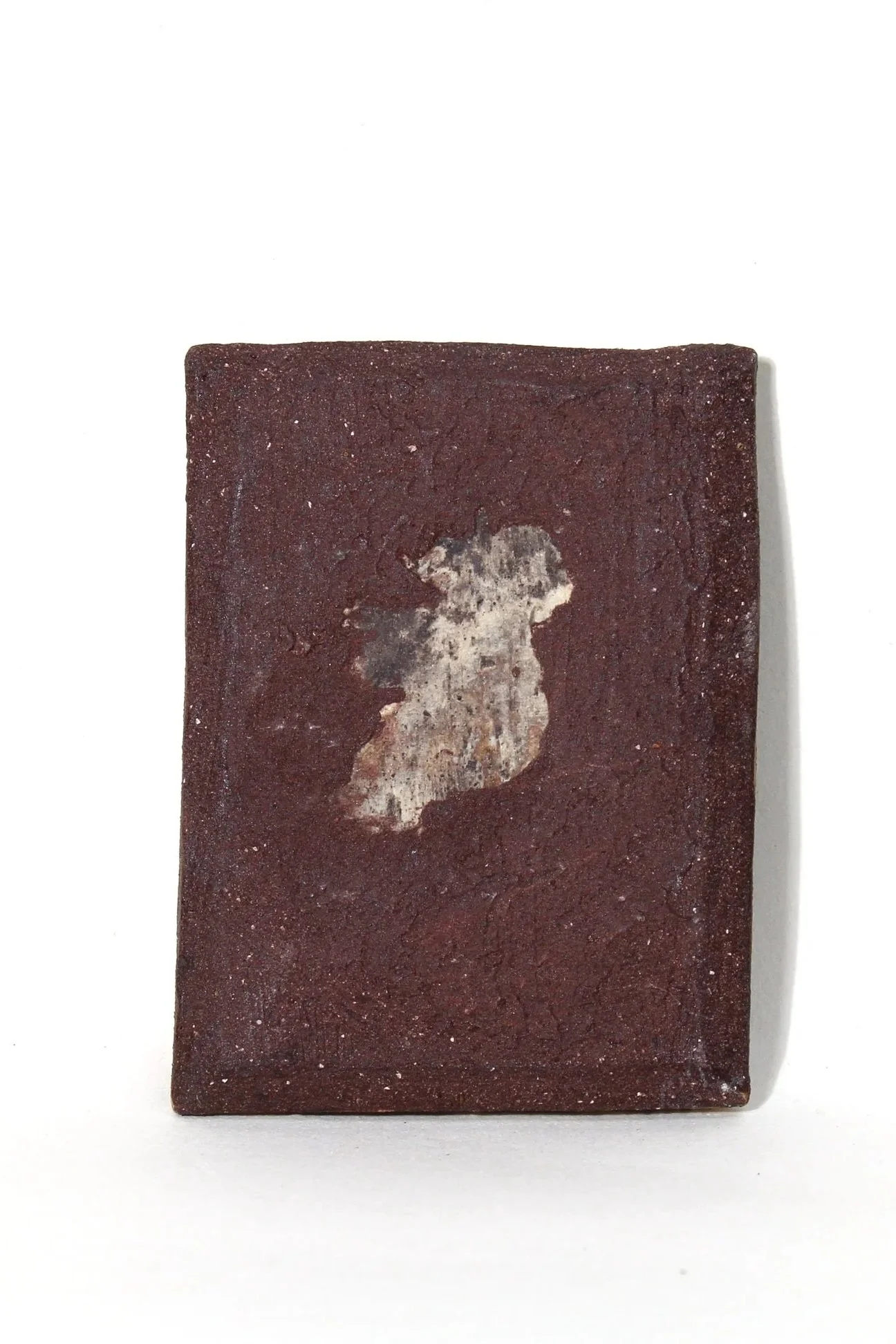 A rectangular clay brick with a white, worn impression of a cat on its surface, placed against a plain white background.