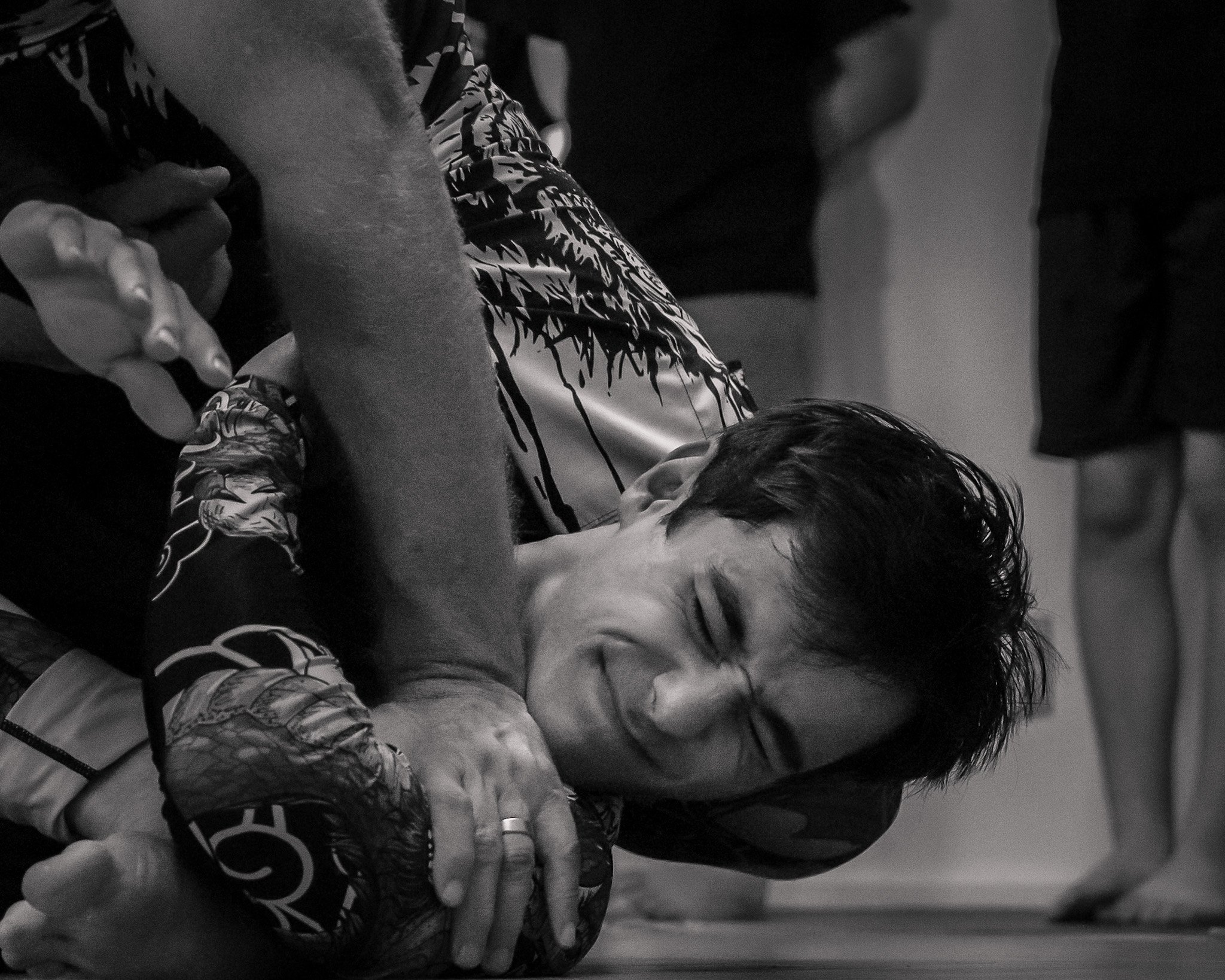 Two people in a grappling match, smiling, with one person underneath and the other on top, both wearing athletic clothing.