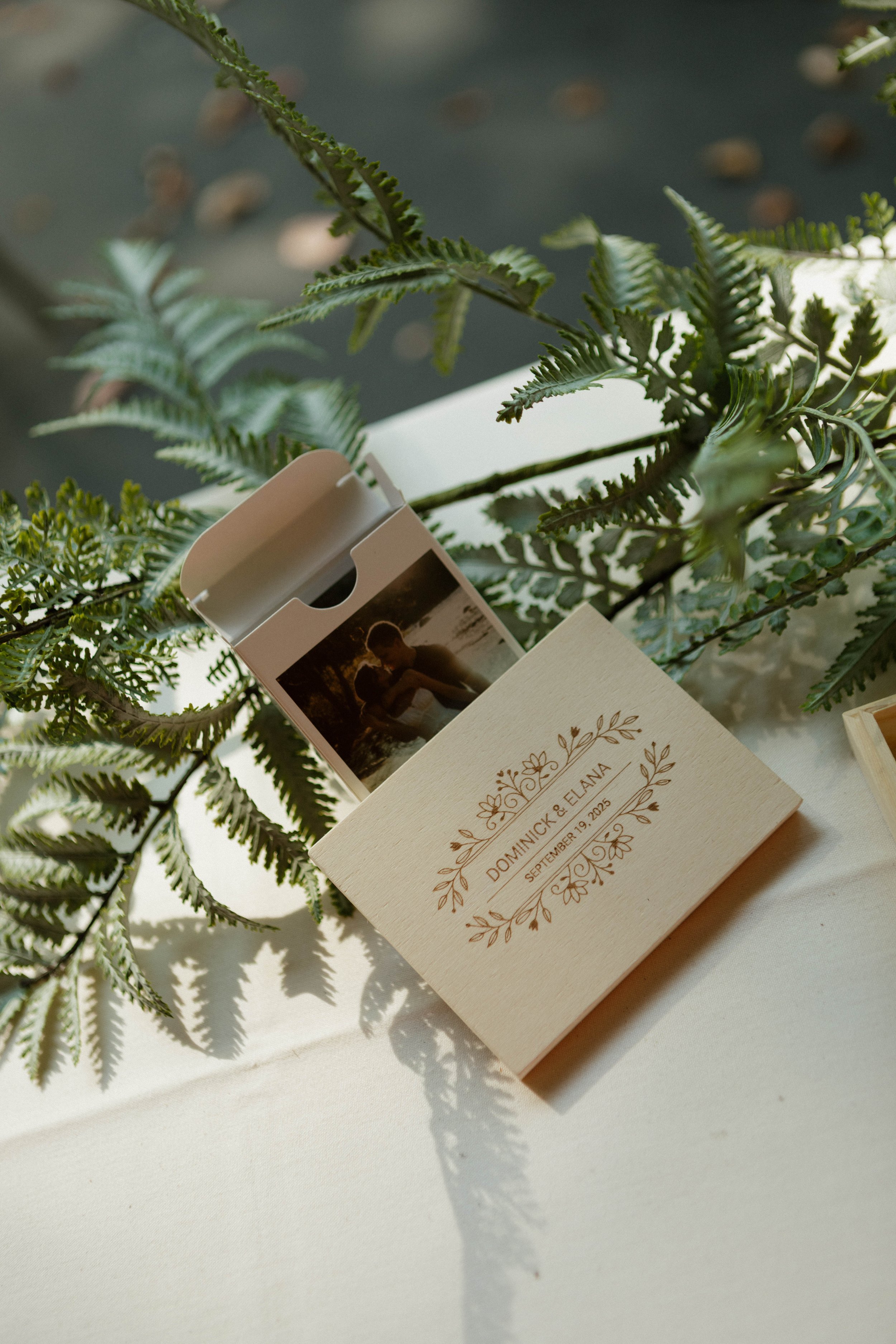 Wedding favor box with a photograph of a couple embracing, surrounded by greenery and labeled with the names Dominnick & Elana and the date September 19, 2025.